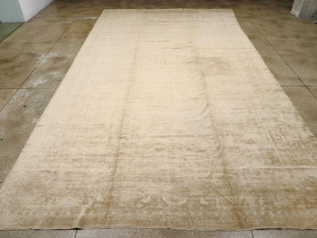 An antique Turkish Oushak oversize carpet. A round light brown medallion is freely placed on a beige ground in this subdued tone-on-tone western Turkish workshop carpet.  No pattern structure hinders the placement of your furniture. And no design