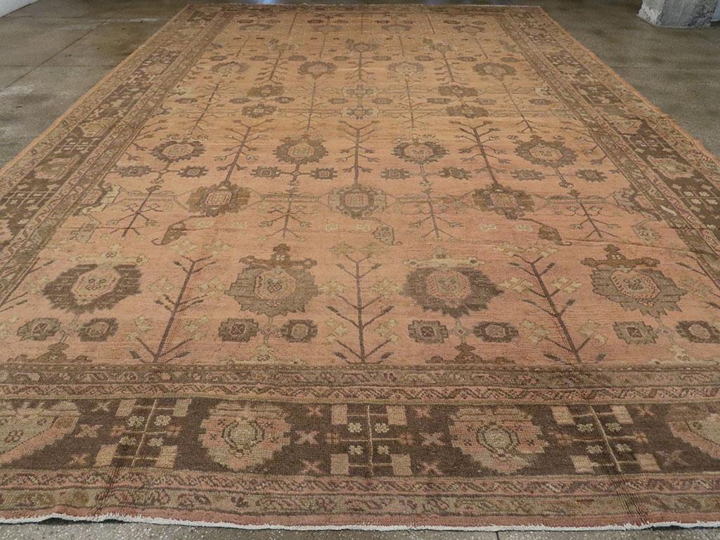 Un ancien tapis turc Oushak surdimensionné. Sept colonnes de palmettes de différents styles délimitent le champ sur un fond de couleur camel. Des feuilles/fleurs stylisées poussent vers le haut à des angles aigus sur les lignes verticales. La