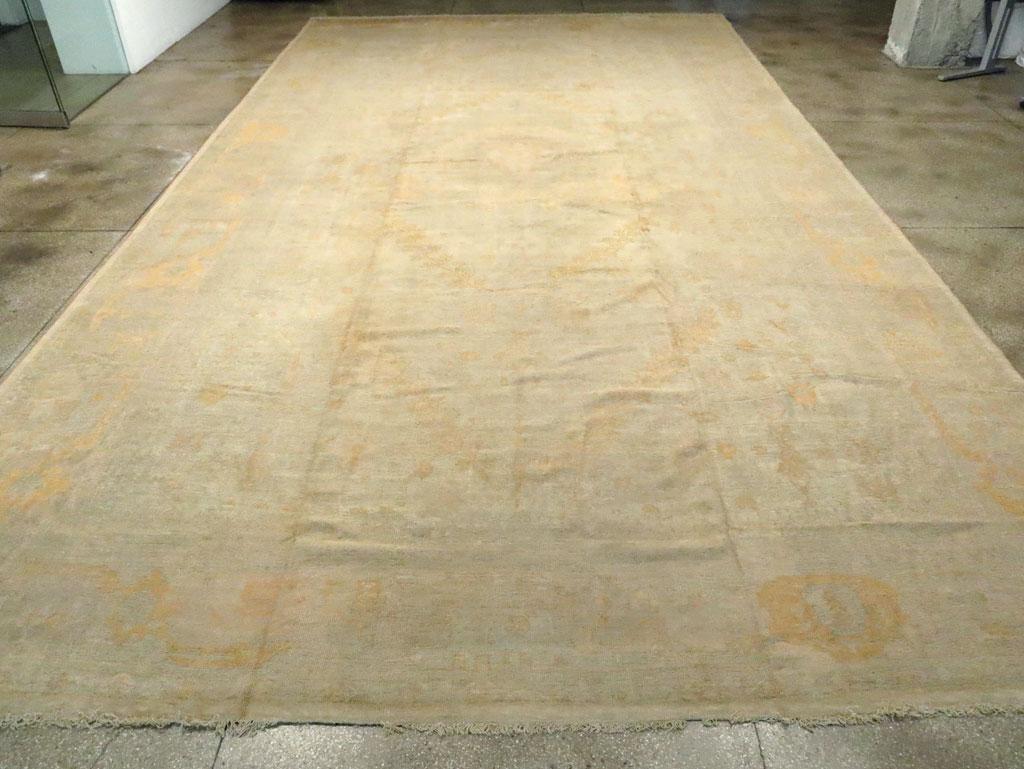 An antique Turkish Oushak oversize carpet. A study in beige and pale gold, this enormous western Turkish workshop carpet must have been a special order for a gigantic room. The semi-open sand field displays a circular medallion between angled,