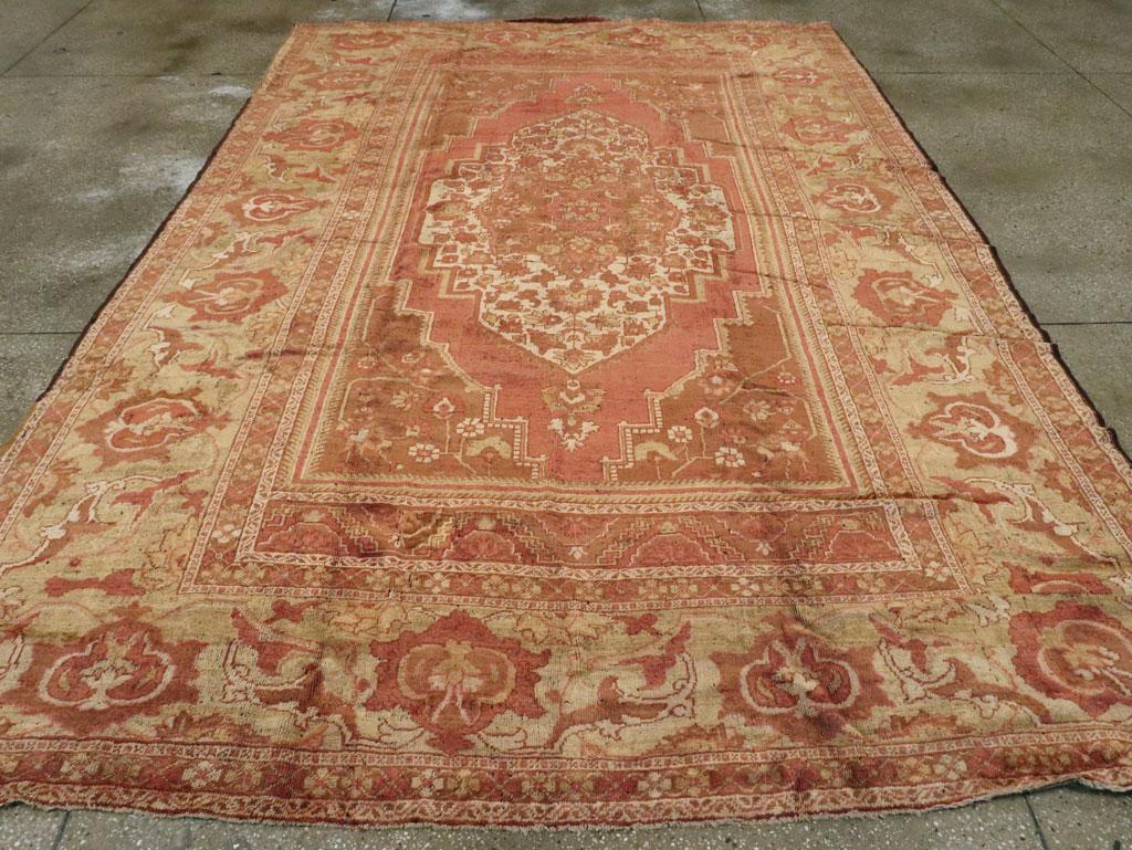 An antique Turkish Oushak room size carpet. An enormous, bold reversing turtle palmette border on a  salmon-buff ground makes a powerful frame for the ivory, flower-filled stepped medallion. The end panels in the field have half-rosettes making a