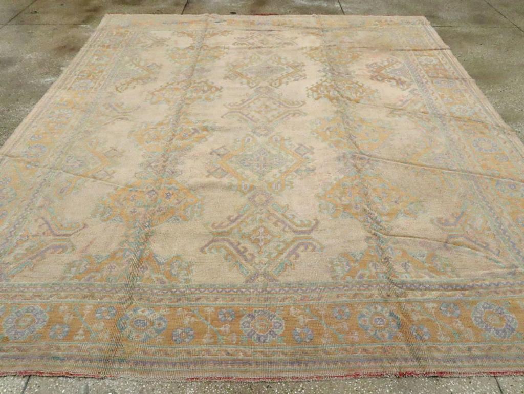 An antique Turkish Oushak room size carpet. Several versions of the foliate lozenge design (Yaprak) are arranged in three full and two half edge columns on the tan field of this west Anatolian all wool construction carpet. The saturated gold tone