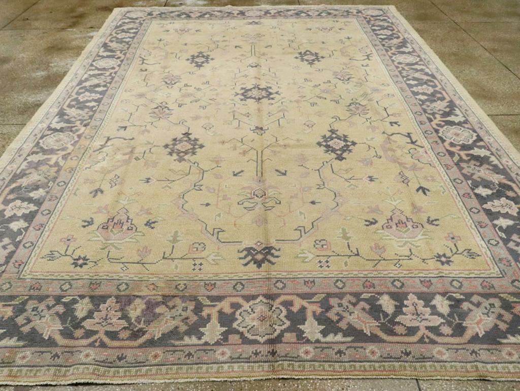 An antique Turkish Oushak room size carpet. This mellow-toned western Turkish workshop room size carpet has a straw yellow field with an allover pattern of super-stylized snowflake rosettes tied together by wiry, angular leafy vines, all framed by a