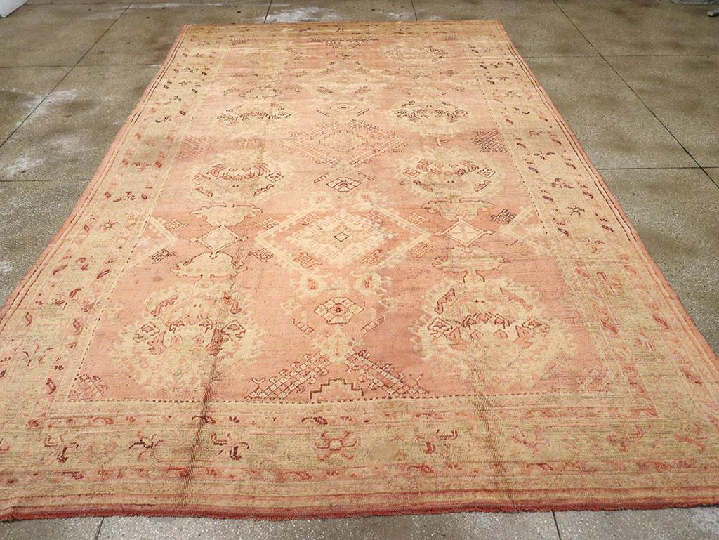 An antique Turkish Oushak room size carpet.The field design of this large-pattern Oushak from western Turkey is spaciously organized around three columns of  Yaprak (“leaf”) lozenges and  ragged palmettes on the salmon-tan field.  The design has