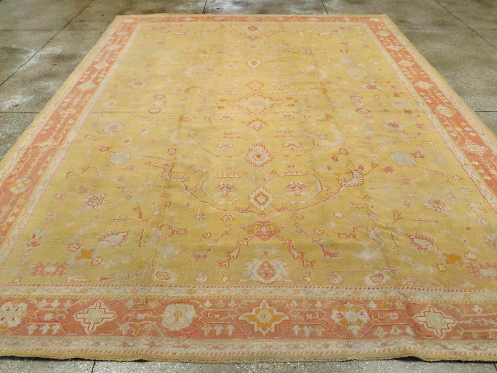 An antique Turkish Oushak room size carpet. Big leaves angularly bend to nearly enclose small palmettes while others reach across the spaciously laid out goldenrod yellow field. The rust border is patterned with a chain of lozenge quatrefoils and