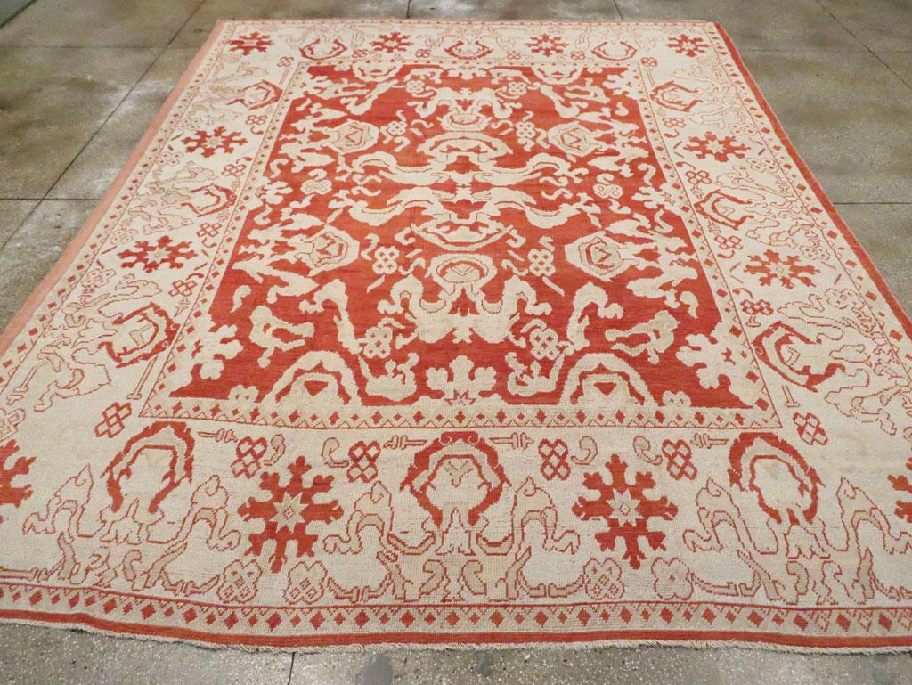 Una antigua alfombra turca Oushak tamaño habitación. Hay bandas de nubes por todas partes en el suelo rojo Turquía de esta alfombra de taller de Anatolia occidental. Más bandas de nubes pueblan el borde principal beige. Todo el efecto recuerda a un