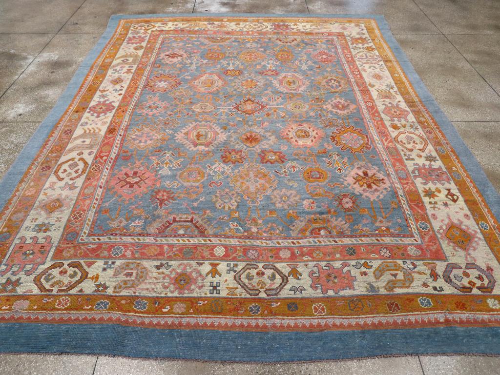 Ein Wollflor aus symmetrischen Knoten auf einer Wollunterlage. Das hellblaue Feld zeigt ein persisches All-Over-Harshang-Muster aus ausgefransten und hakenförmigen Polygonen, die an zerfranste Palmetten erinnern. Der Querbalken ist durch eine