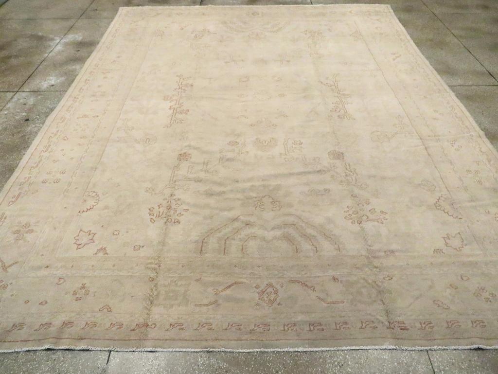 Una antigua alfombra turca Oushak tamaño habitación. El campo beige de esta alfombra turca occidental, esencialmente tono sobre tono, tiene un medallón abierto transparente flanqueado verticalmente por grandes plantas con hojas hacia abajo. Los