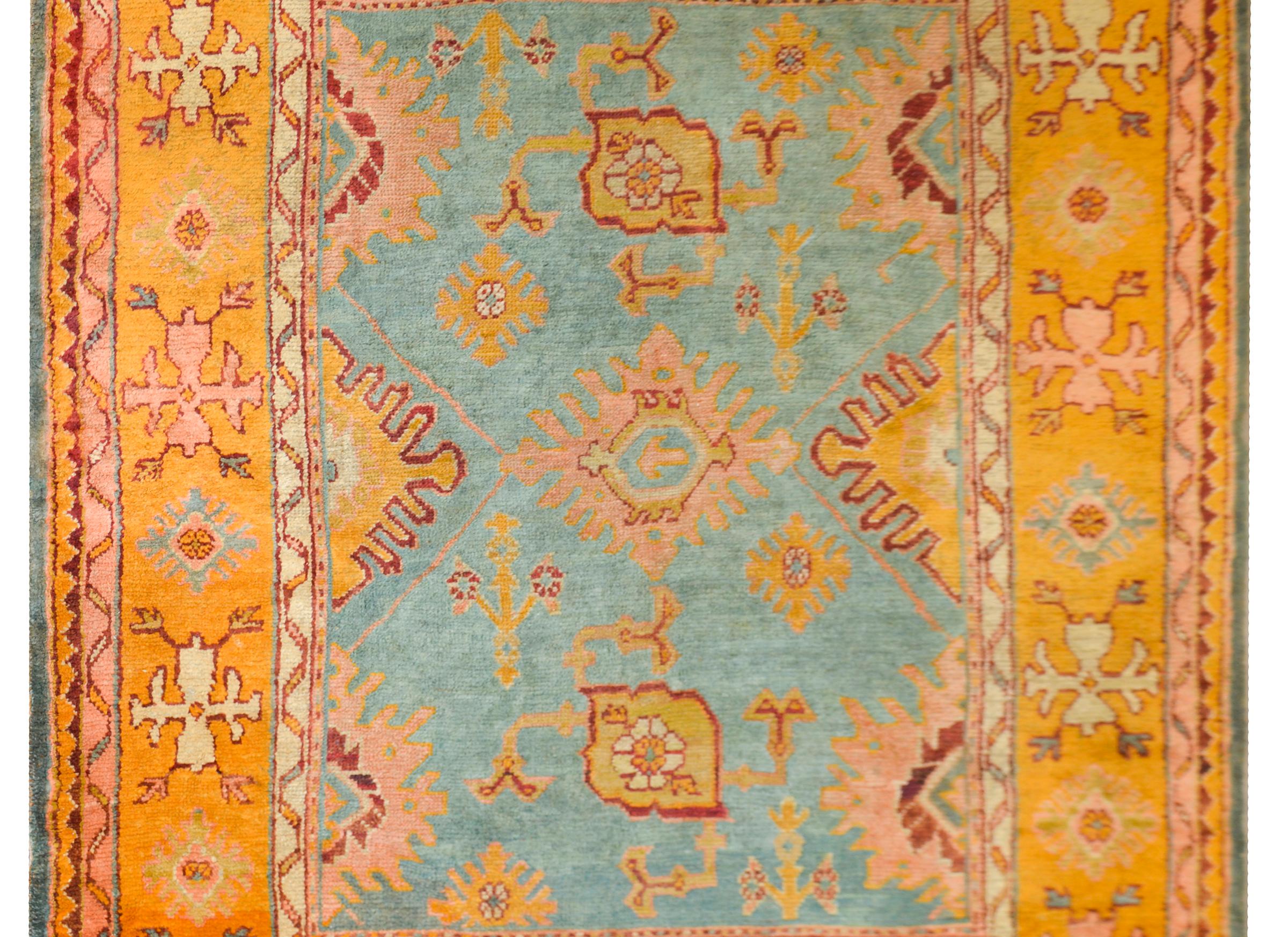 An exciting and bold early 20th century Turkish Oushak rug with a wonderful large-scale stylized floral patterned field woven in gold, crimson, and salmon, and set against a light turquoise blue field. The border is exceptional with a wide stylized