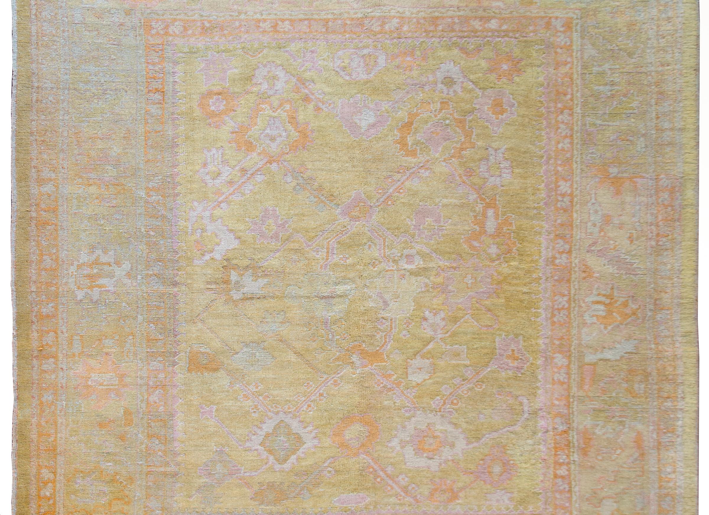 A stunning early 20th century Turkish Oushak rug with a beautiful large-scale stylized trellis floral pattern with pink, orange and yellow flowers and pink and white vines, all set against a gold background and surrounded by a border composed of