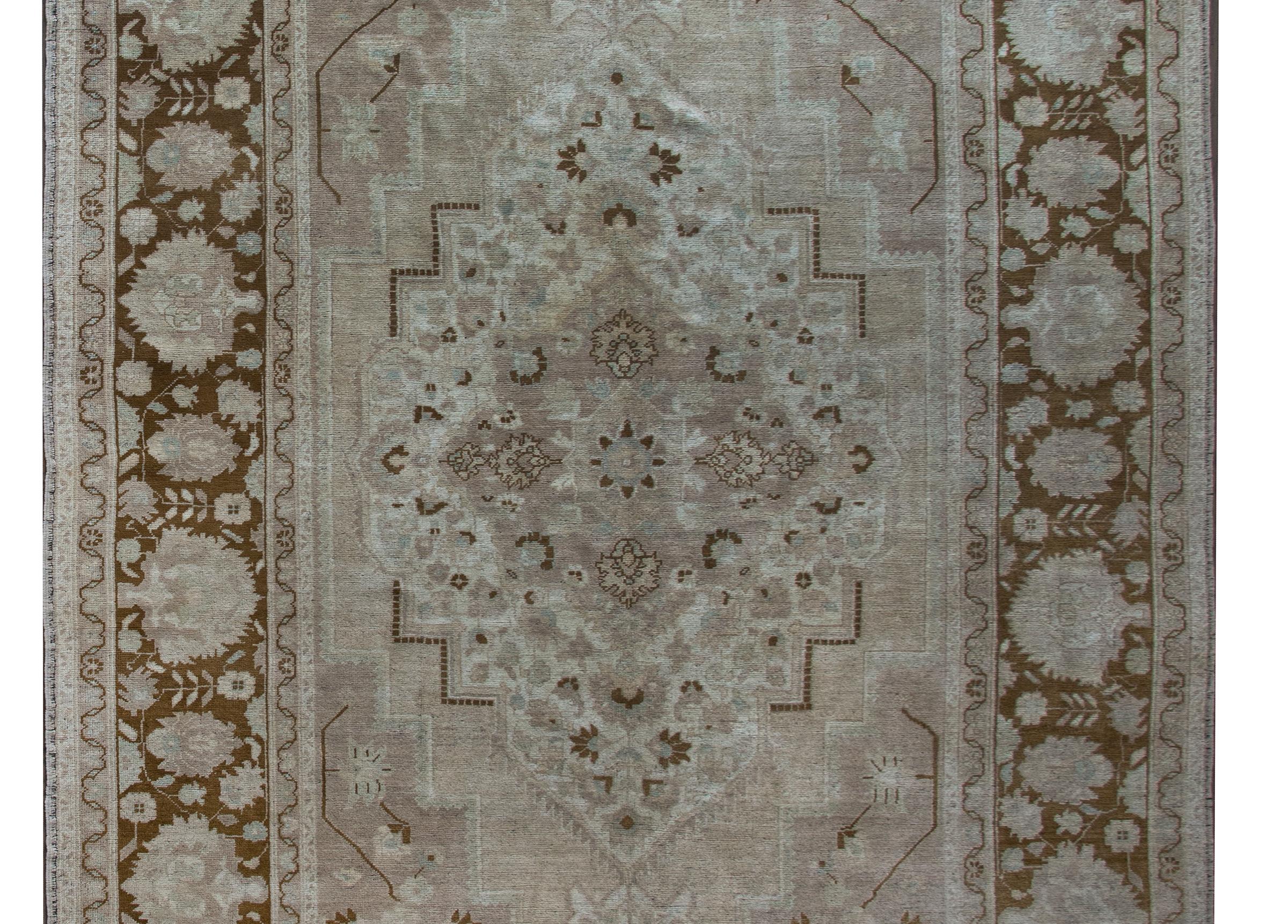 A wonderful early 20th century Turkish oushak rug with a beautiful floral medallion living amidst a field of more flowers and surrounded by a wide large-scale floral and scrolling vine pattern. This rug has been given an antique wash to mute the
