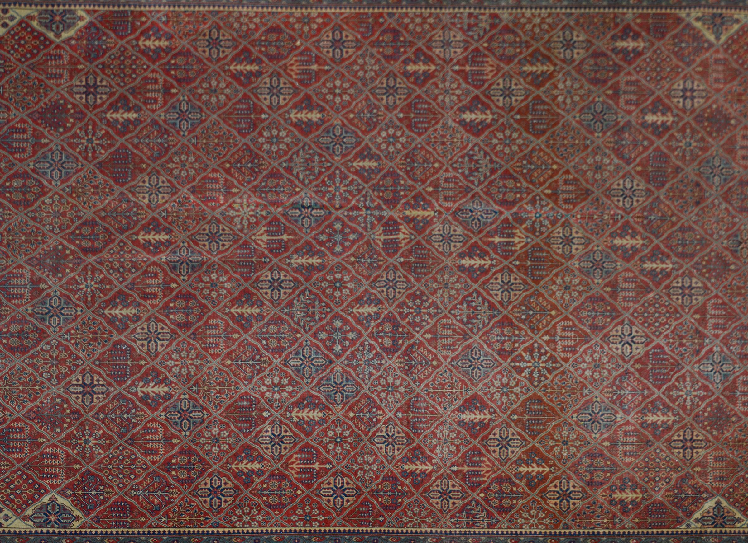 An early 20th century Turkish Sivas rug with the most wonderful woven patchwork and trellis pattern containing myriad trees-of-life and flowers all woven in light and dark indigo, cream and pink, and set against a crimson background. The border is