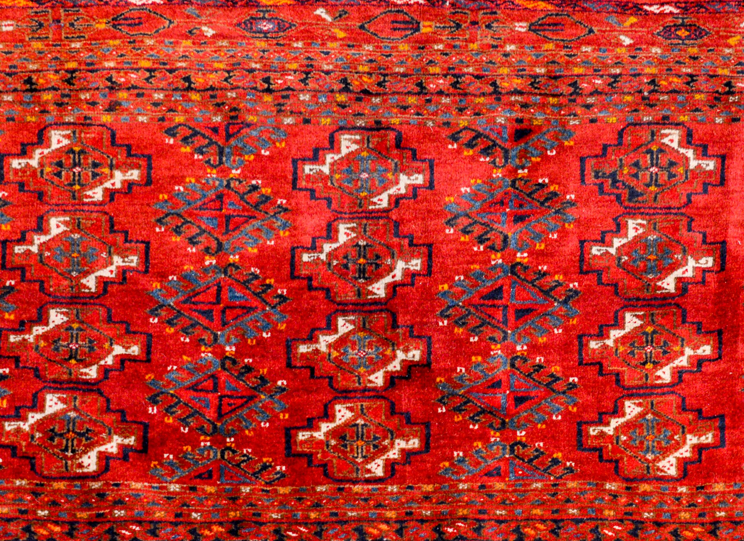 A wonderful early 20th century Persian Turkoman bag face rug with a beautiful all-over pattern of stepped diamonds woven in white, orange, and black wool, on a bold crimson background. A sweet border with trees and other stylized flowers surrounds
