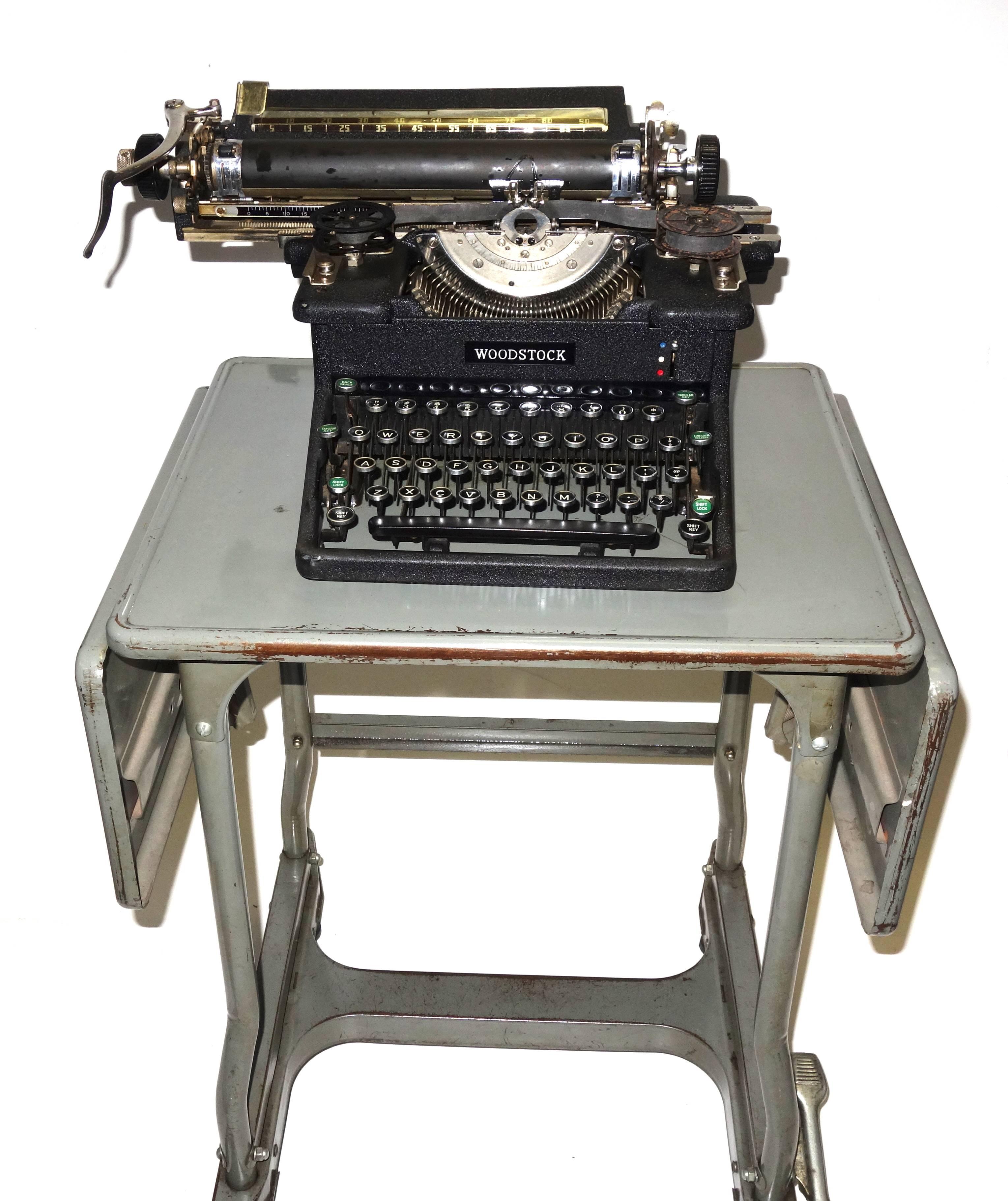 Offered for your consideration is this iconic, working, circa 1920s Woodstock vintage typewriter displayed on a vintage steel typewriter drop leaf rolling table.
Woodstock was based near Chicago and started out as the Emerson Brand, then the Roebuck