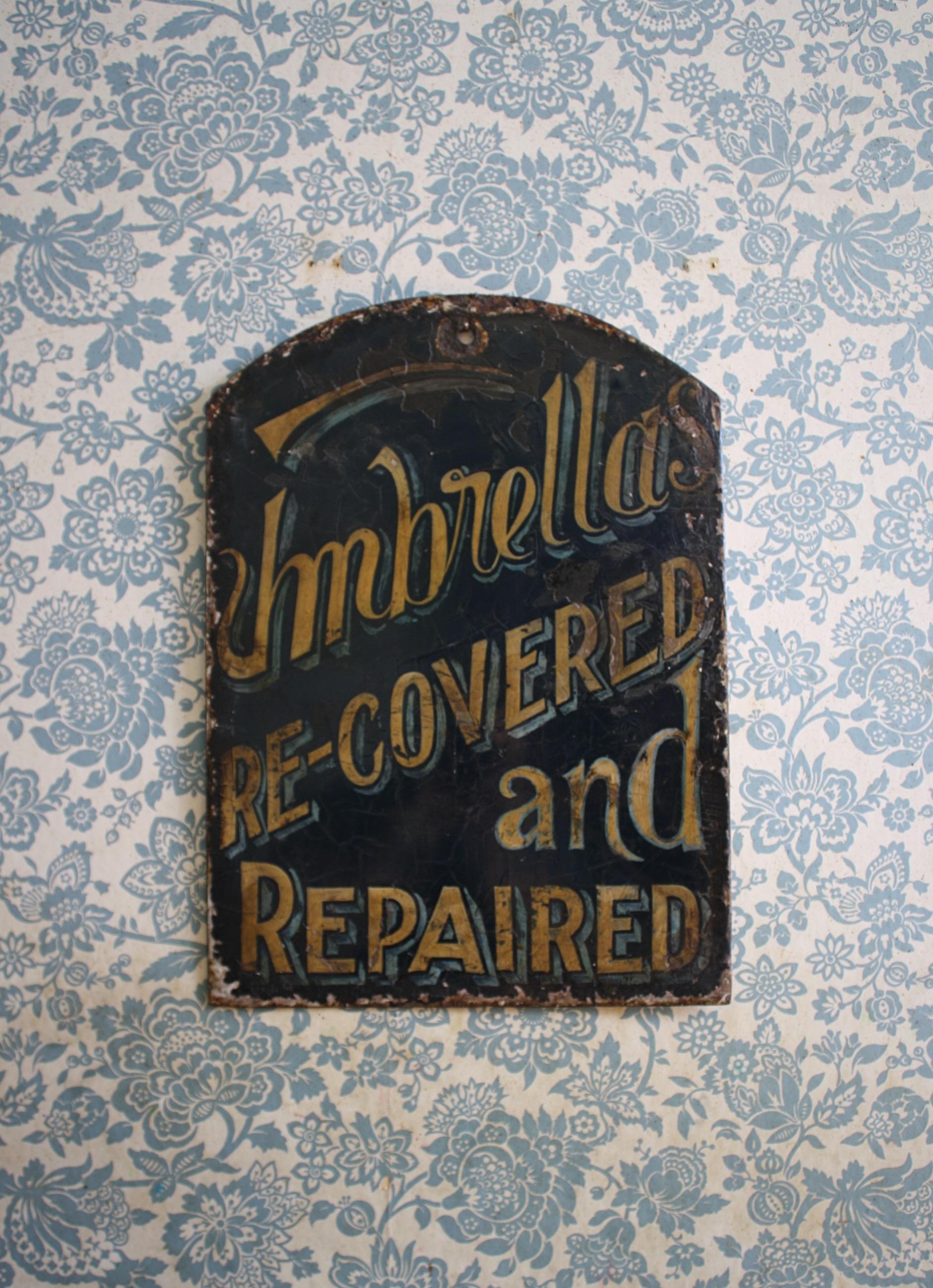 A atheistical pleasing trade sign from the early part of the 20th century. 

On a dark blue ground with a contrasting yellow and light blue changing script in font perspective and size reads Umbrellas Re-Covered and Repaired.

This has been
