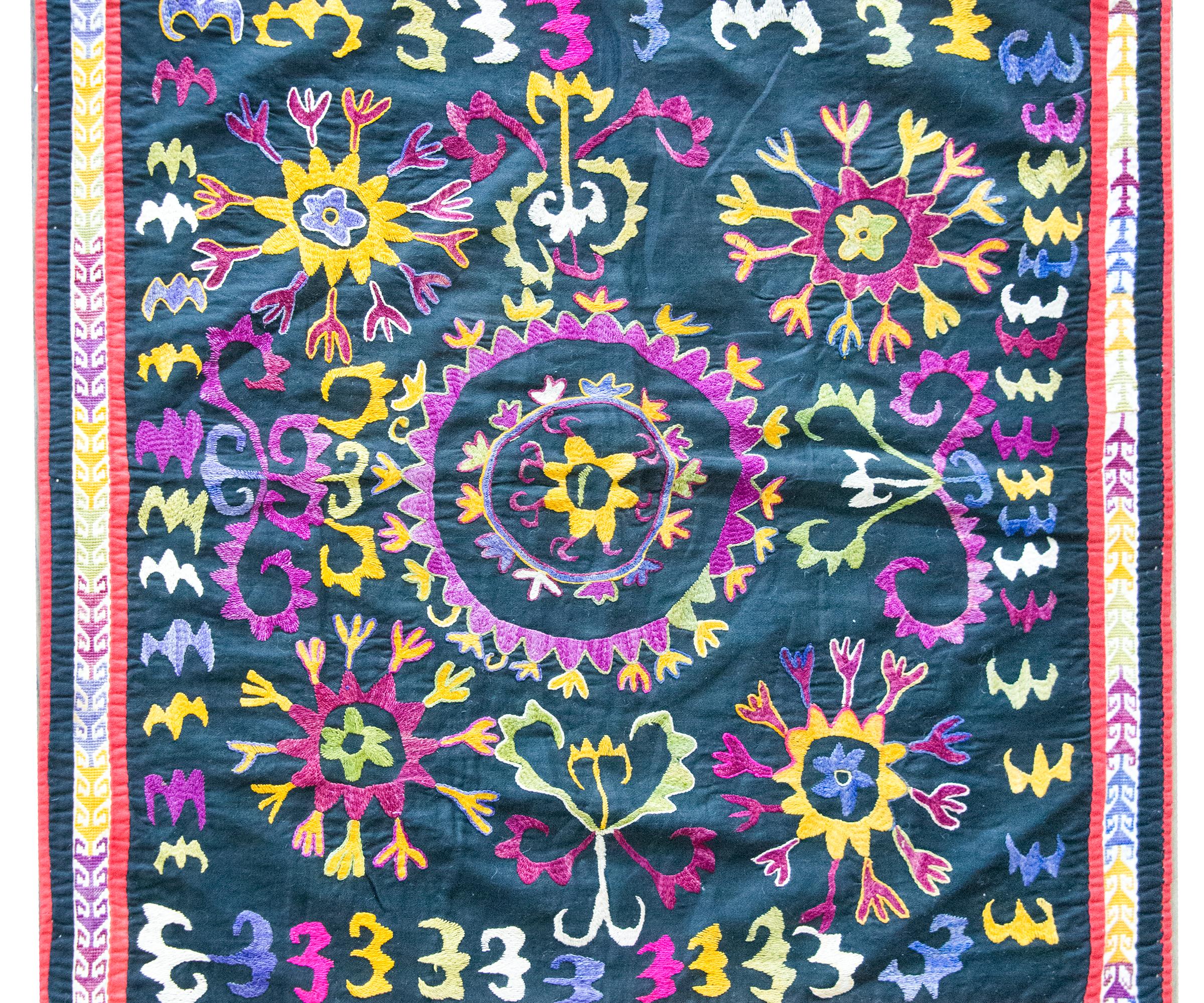 Ce Suzani ouzbek du début du XXe siècle est un exemple frappant de l'art textile d'Asie centrale, riche en couleurs et en significations. En son centre s'épanouit un médaillon floral éclatant, entouré d'une constellation de grappes florales