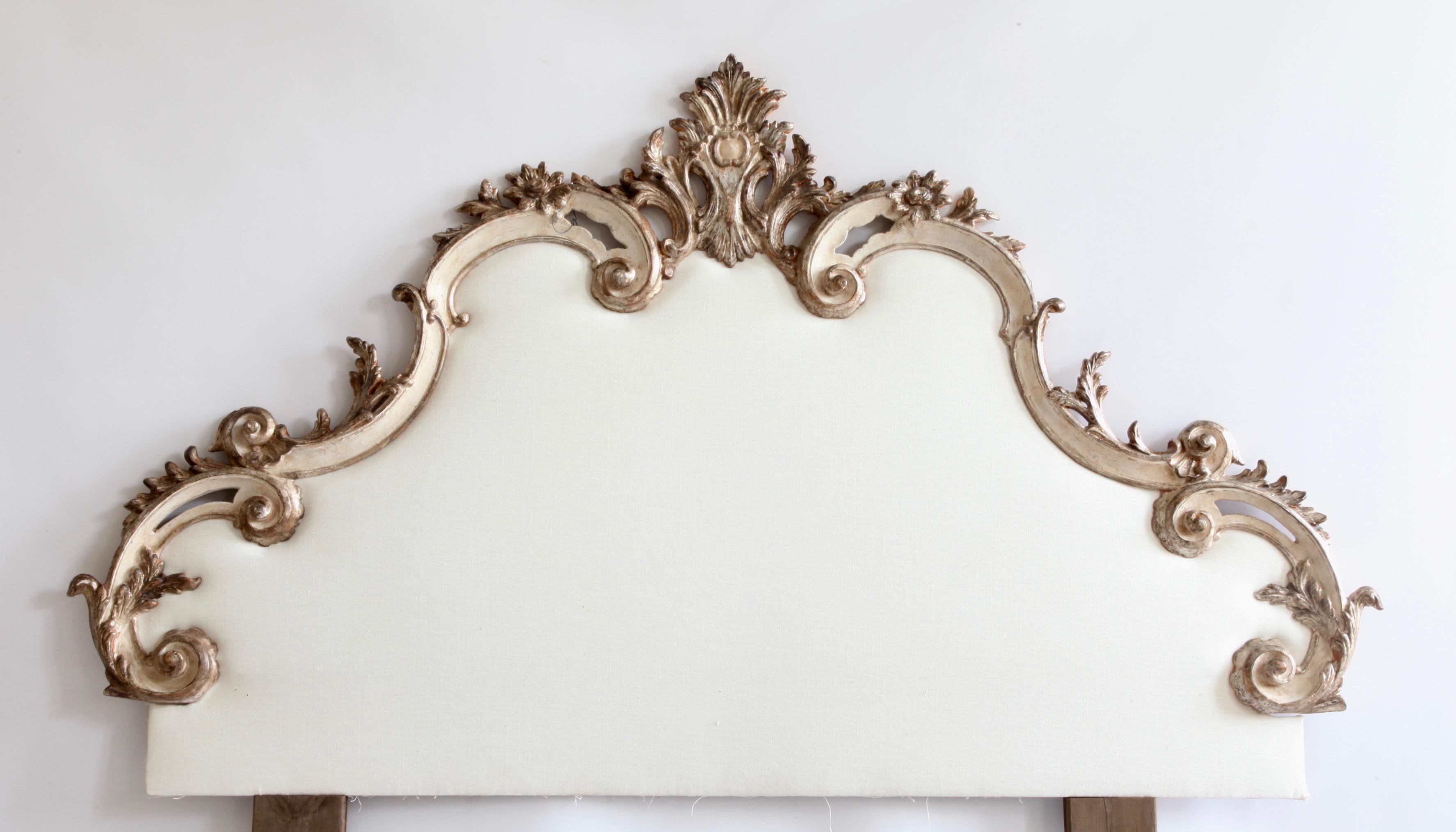 This early 20th century, hand carved headboard from Venice, Italy, is finished in an old, taupe, white patina, enhanced by hand gilded, silver highlights. The carving consists of sweeping, deep scrolled, 's' curves and decoratively carved accents of