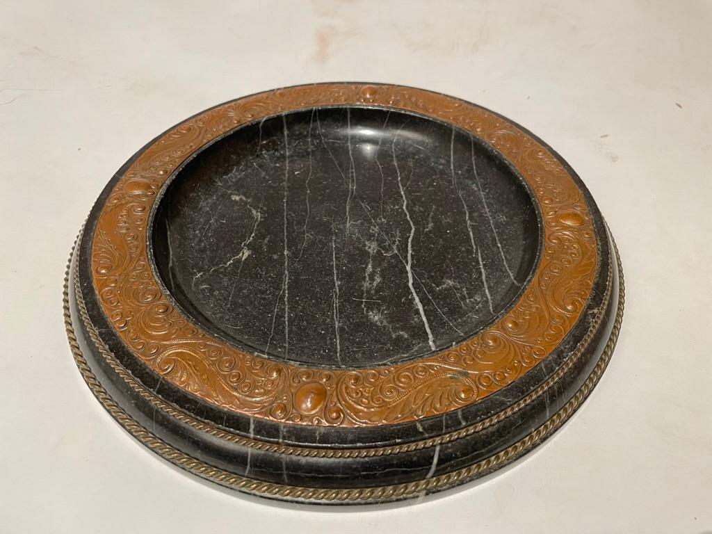 Plato austriaco belga de mármol negro con una maravillosa banda repujada de cobre con decoración típica de la Secesión vienesa, que evoca el fondo de un cuadro de Gustav Klimt. Es probable que originalmente fuera un plato para tarjetas de visita,