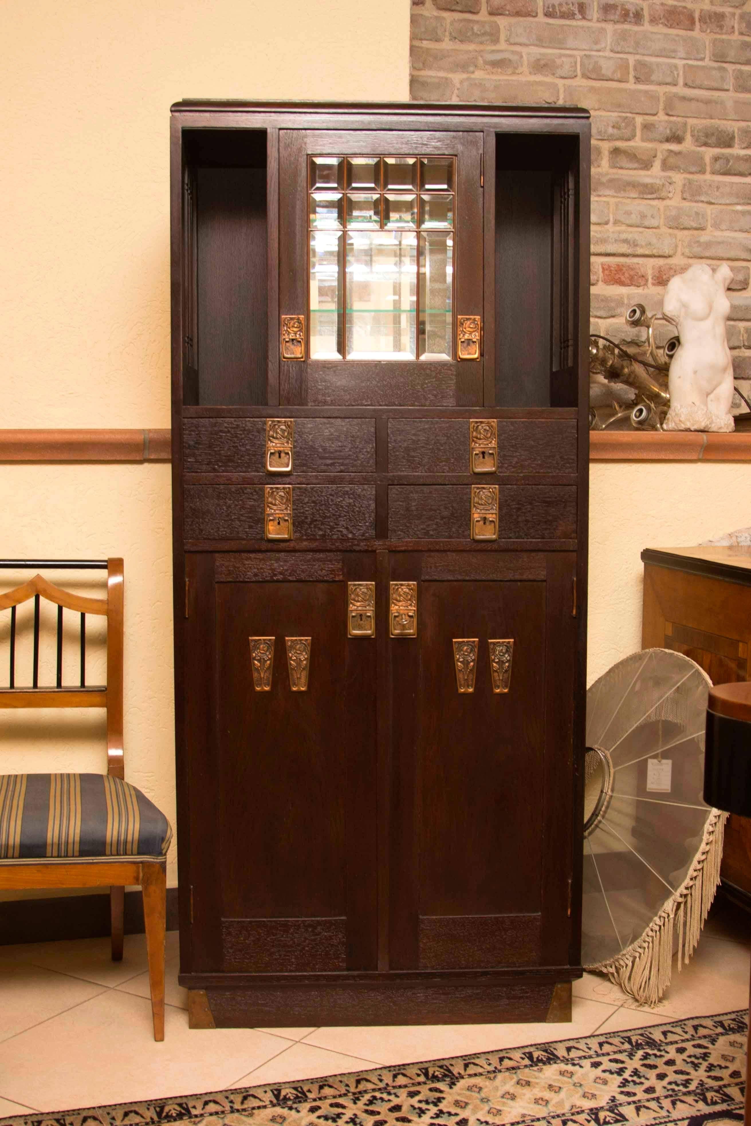 This Secession cabinet was produced in Austria-Hungary, circa 1910. It is made of oak wood. It features a glazed upper part with a bar and a beautiful brass fittings with decorative Art Nouveau elements. The side parts features a pillars typical for