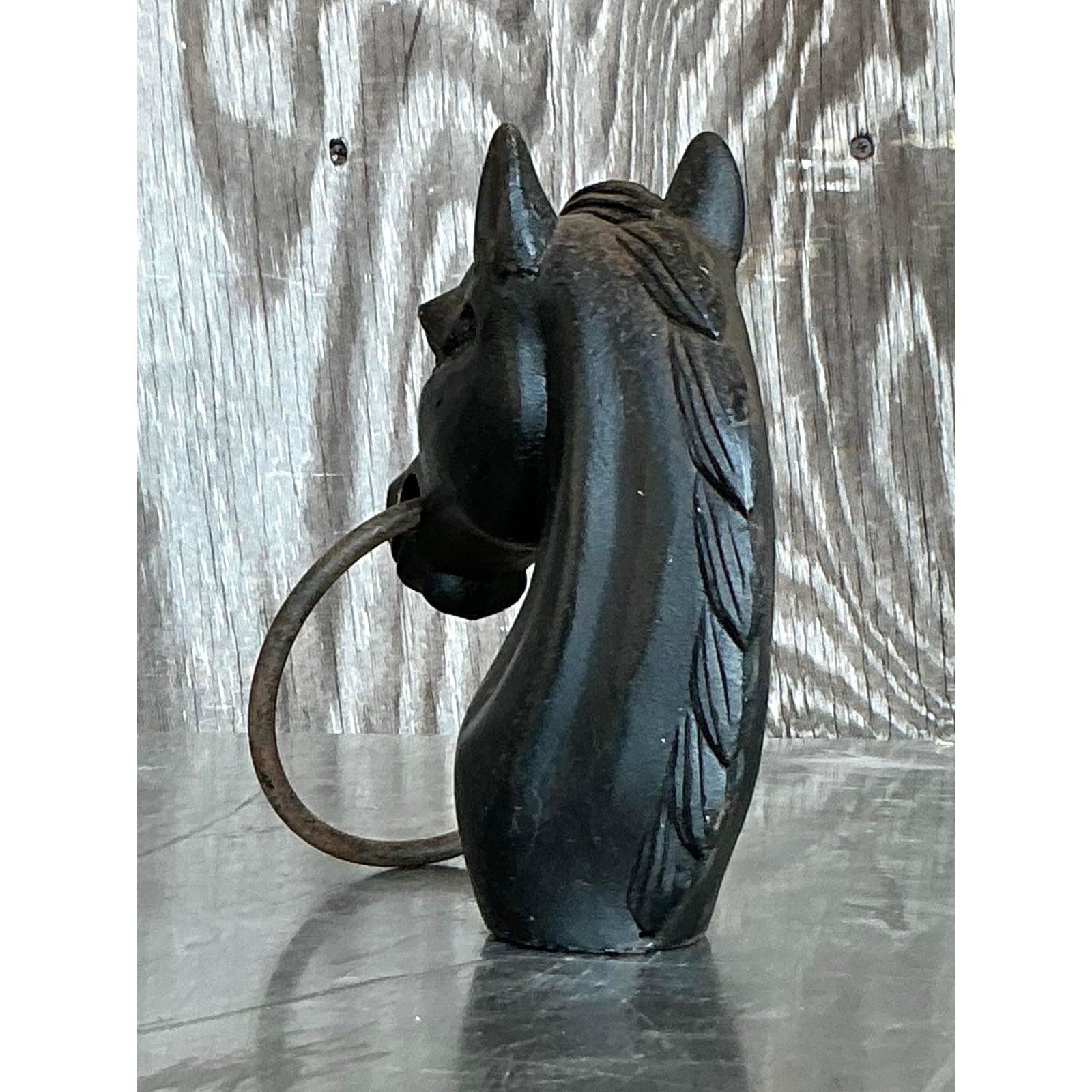 Aggiungi un tocco di robustezza americana al tuo arredamento con questa suggestiva testa di cavallo vintage in ferro battuto. Scolpito con linee decise e dettagli espressivi, questo pezzo in ferro annerito presenta un classico anello che attraversa