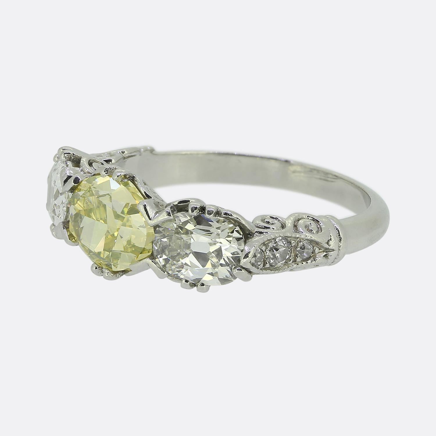 Nous avons ici une captivante bague à trois pierres méticuleusement fabriquée en platine au début du 20e siècle. Au centre du visage se trouve un diamant jaune-vert vif, de forme ovale, qui rayonne d'une lumière chaude. Deux diamants ovales à
