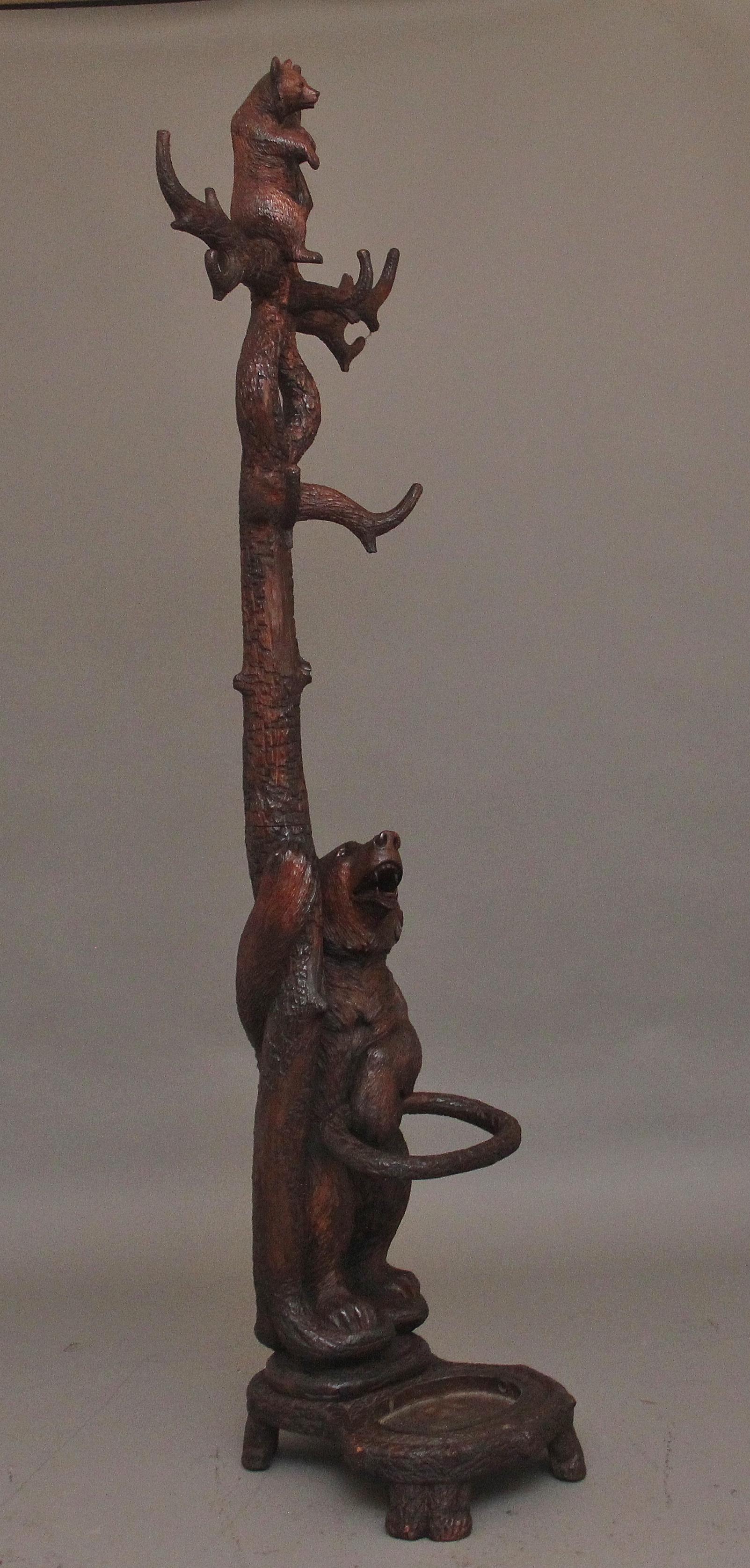 A finely carved early 20th Century walnut black forest bear hall stand with a cub playing in the branches above, the bear below looking up and holding and standing on an umbrella stand, the construction is very sturdy and the branches are more than