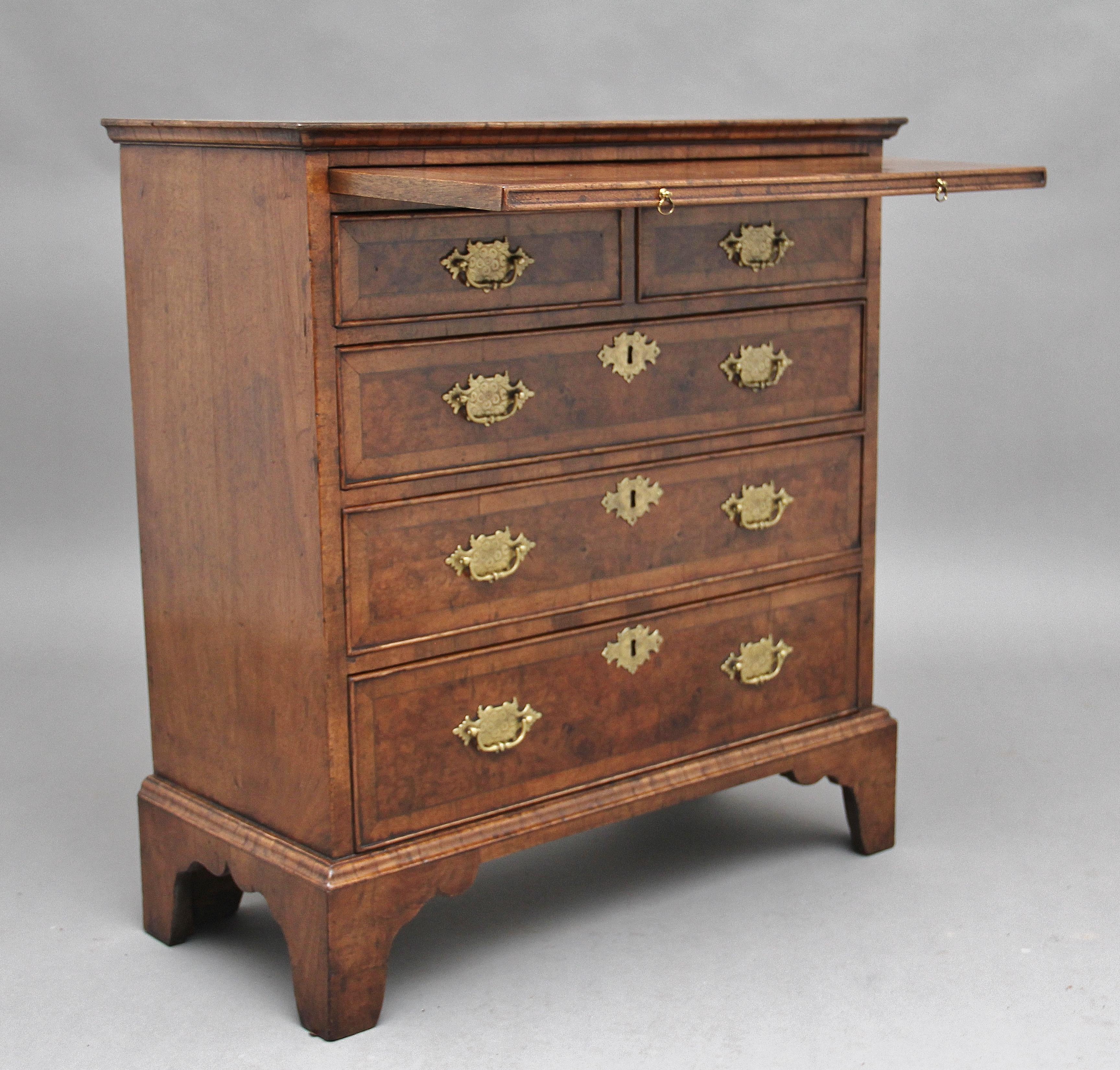 Early 20th century walnut chest of drawers, the crossbanded rectangular top above a brushing slide, with two short over three long graduated drawers with brass plate handles and escutcheons, the drawers fronts also crossbanded, standing on bracket