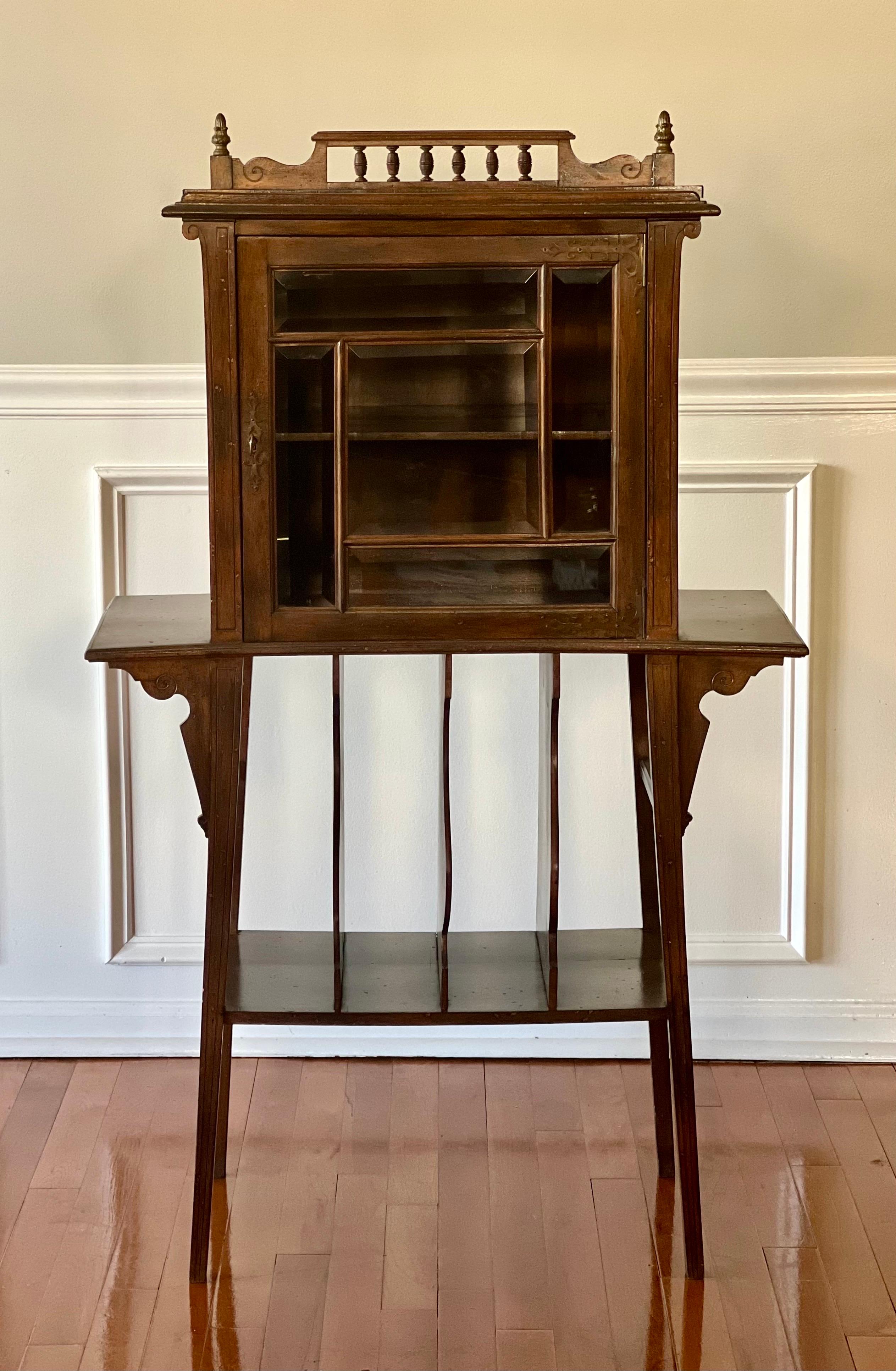 Late Victorian walnut music Canterbury cabinet with stand, early 20th century.

Set upon straight splayed legs, this charming stand features a lower partitioned shelf, six-pane beveled glass door and galleried top with bronze finials. The interior
