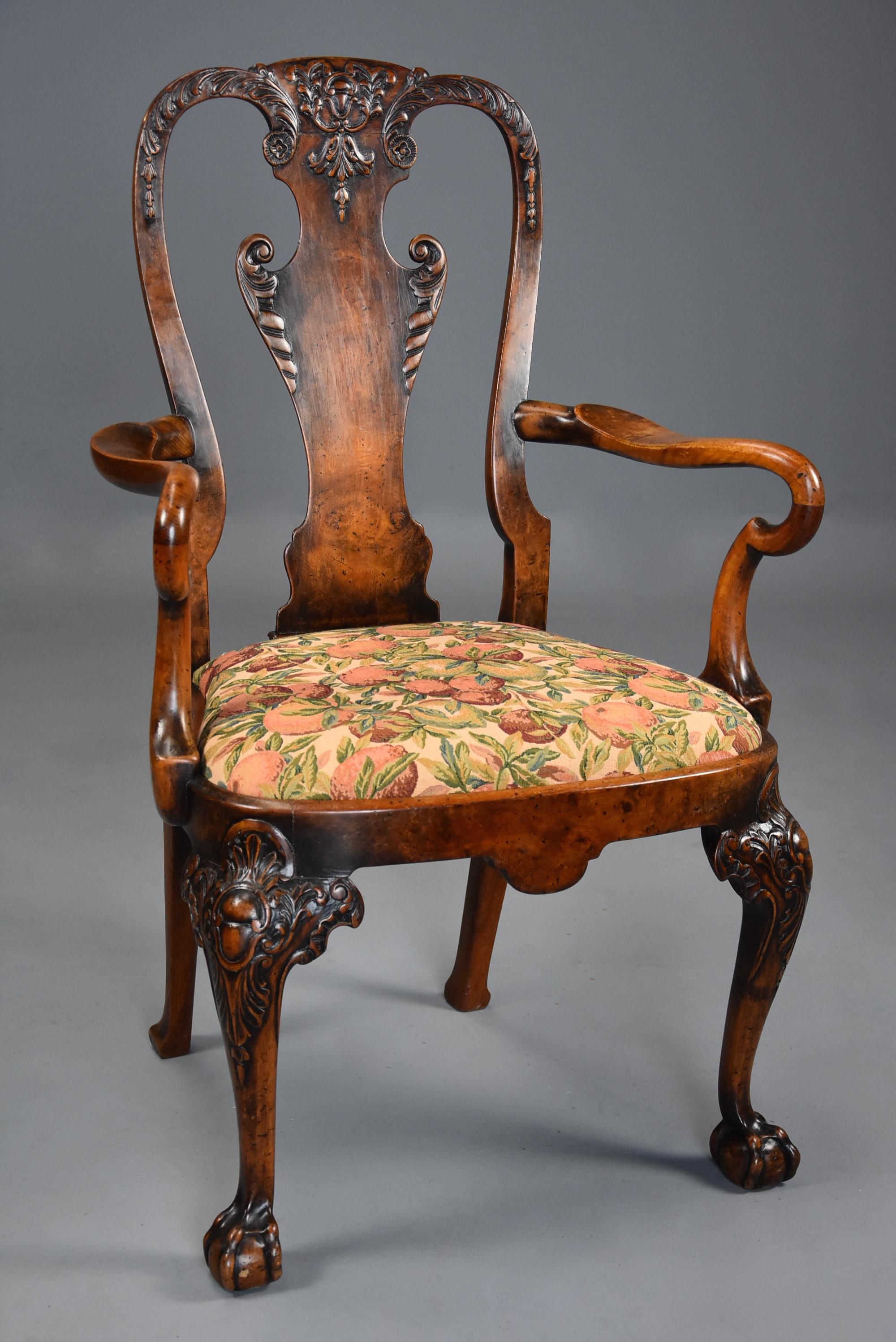 An early 20th century walnut open armchair in the Queen Ann style of fine patina.

This finely executed armchair consists of a shaped back with floral, foliate and scroll carved decoration with central burr walnut veneered back splat with carved