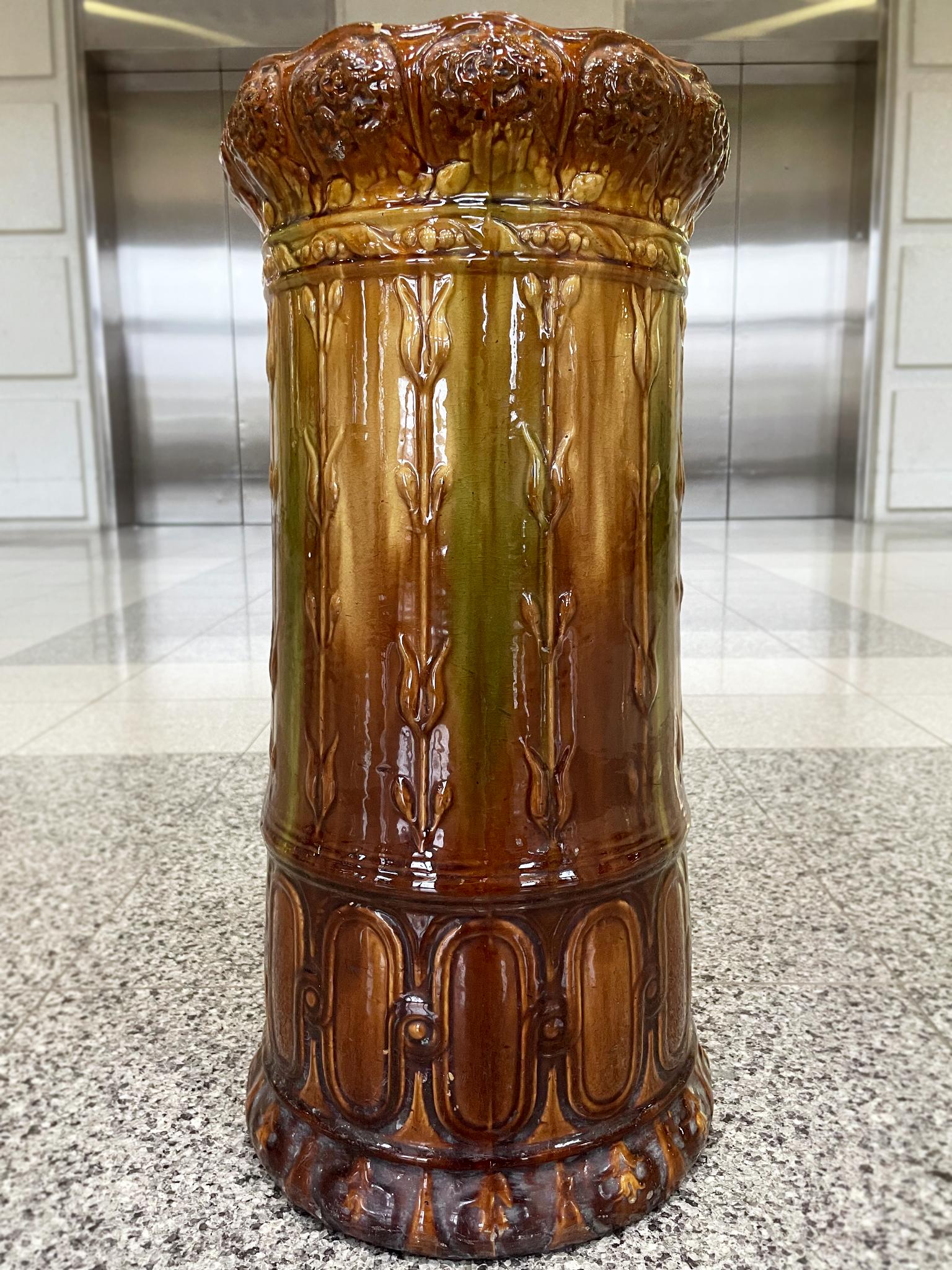 A ceramic umbrella stand made by Weller Pottery in the early 20th century. It's remarkable for its beautiful glazing with craquelure and gradations of color that go from ocher yellow to burnt umber hues. The shape makes use of floral motifs that