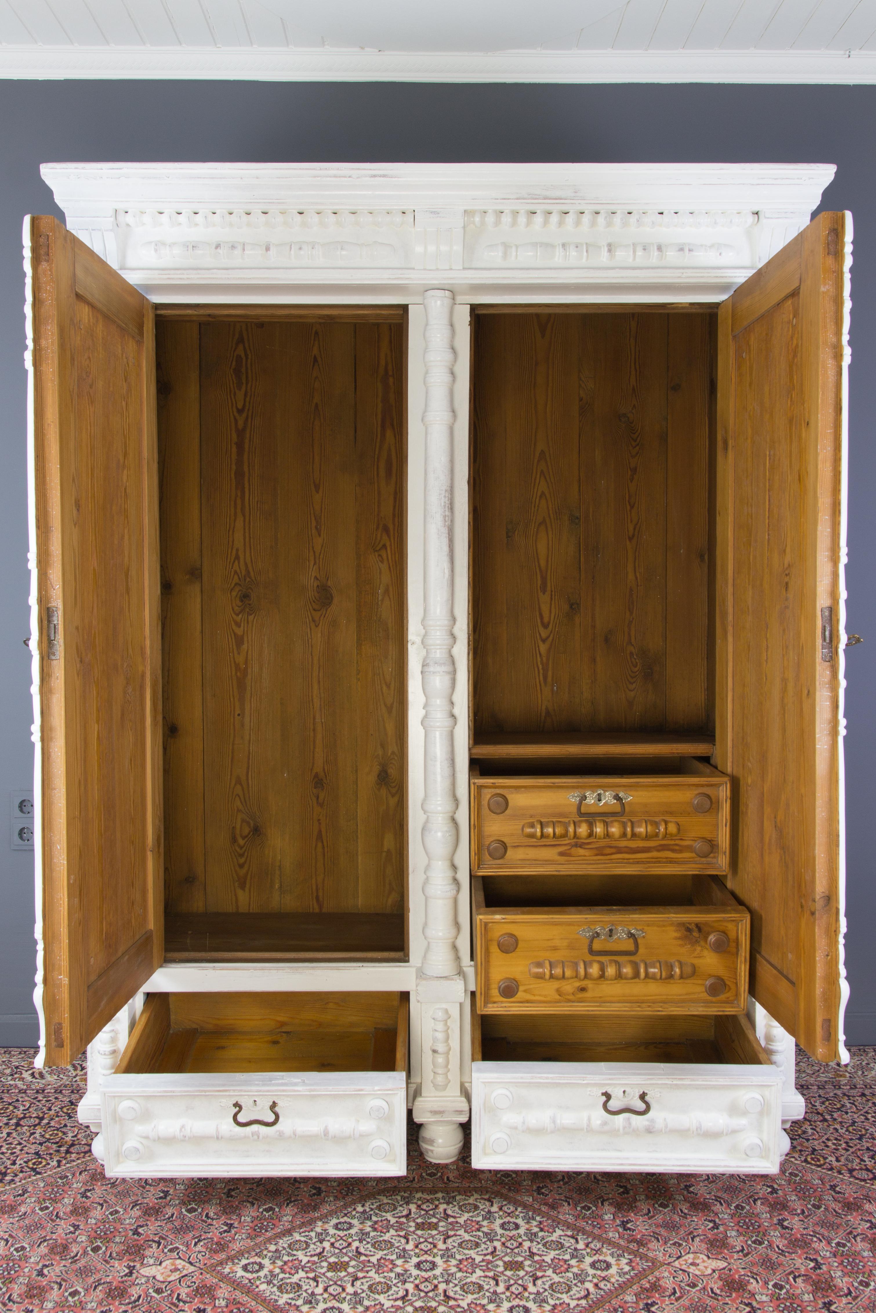 This beautiful and massive early 20th-century Baltic armoire features paneled doors and two pull-out drawers below, three massive turned column pilasters, and two half-columns on each door. The exterior front side has a whitewashed finish. Inside,