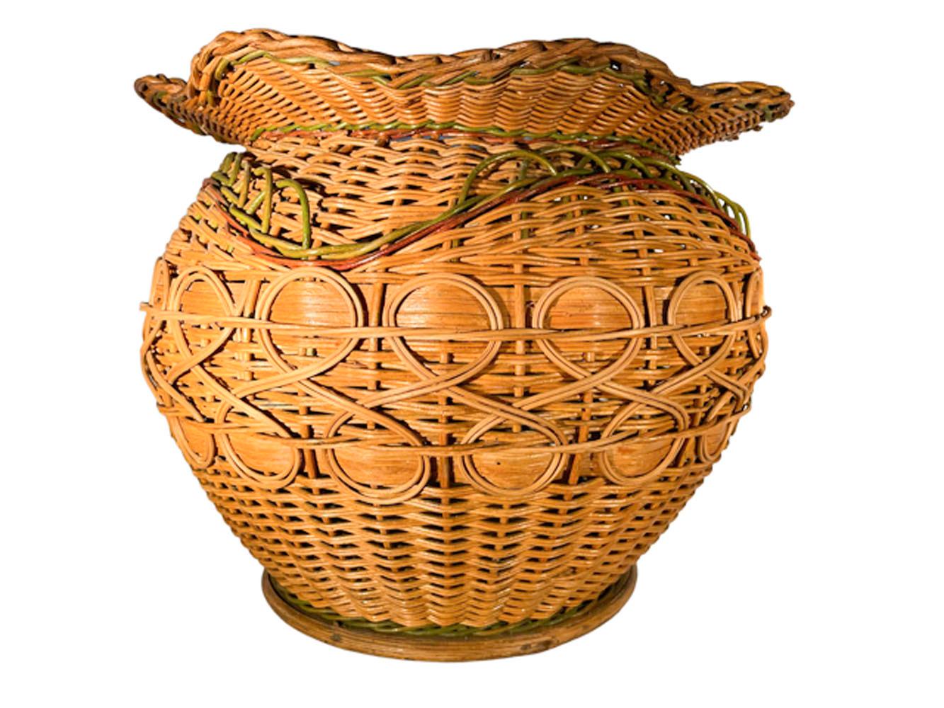 Large, early 20th century, wicker cachepot / planter of circular form with a serpentine rim woven in natural cane and decorated with red and green colored cane as well as woven detail all set on a wood base. Excellent Condition. 

Overall:
11.5