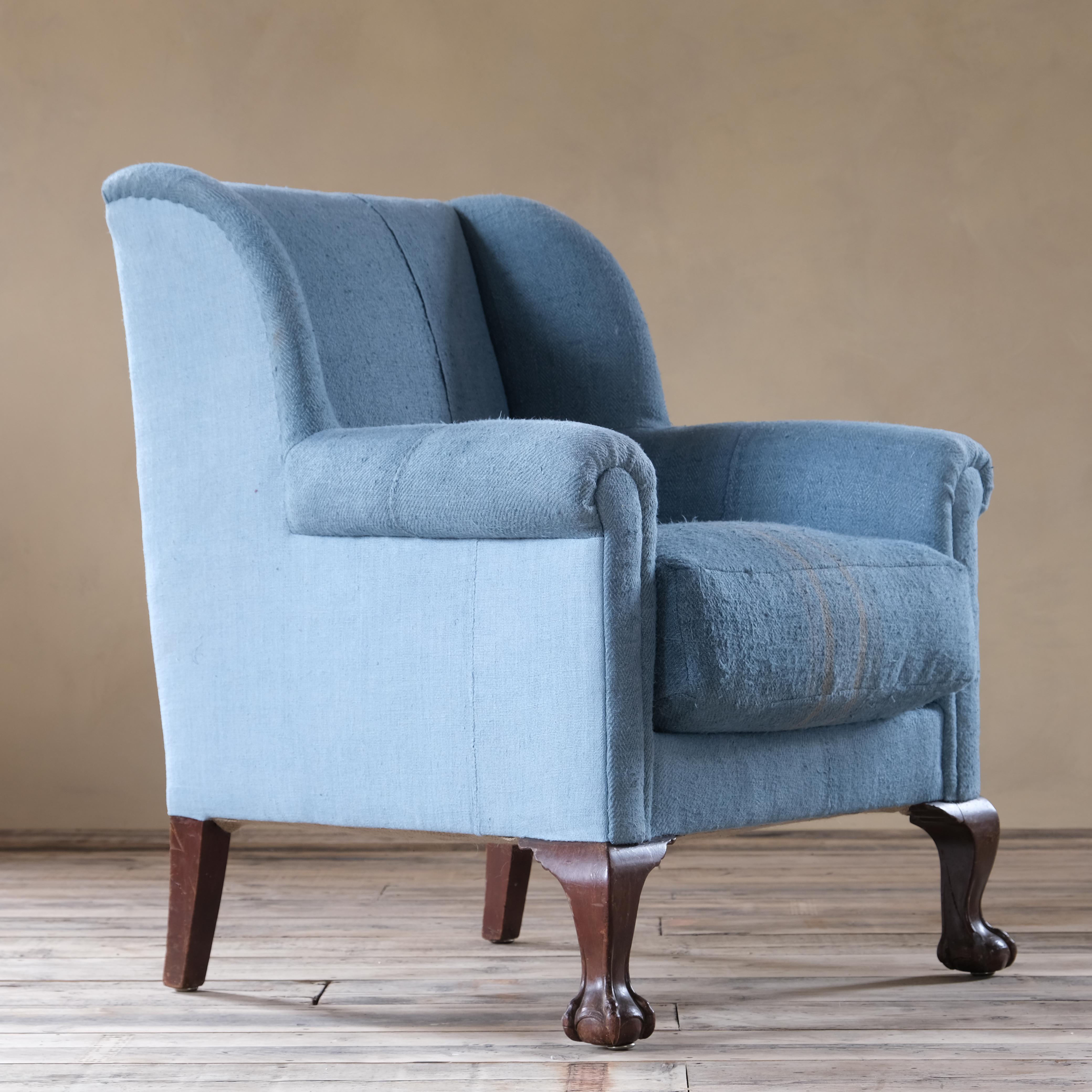 An early 20th century wingback armchair raised on mahogany ball and claw front legs and upholstered in sky blue contrasting antique grain sacks hand dyed using traditional methods. 

81cm wide
81cm deep
95cm high
45cm seat height.