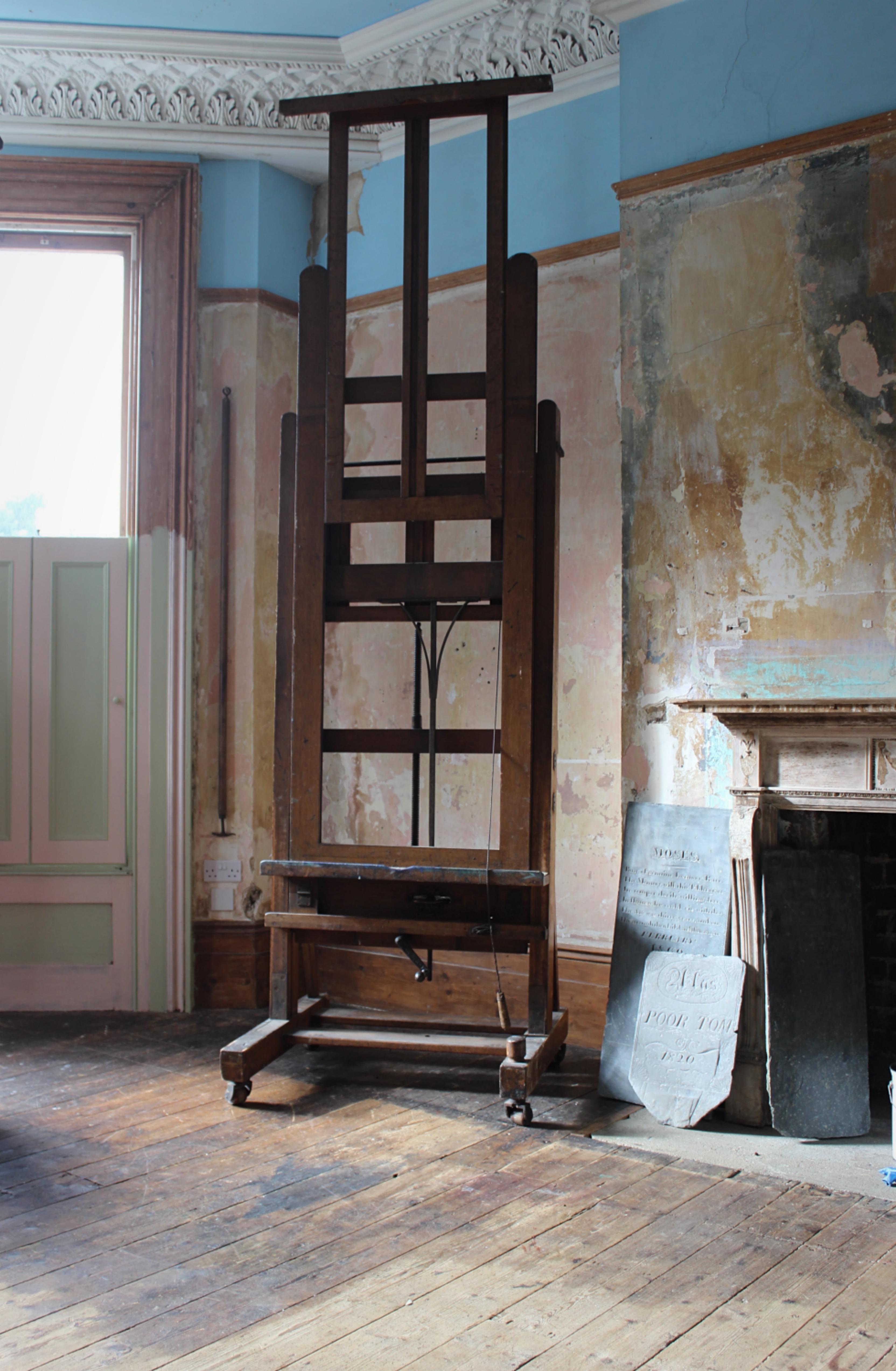 A large and impressive studio artist easel by Winsor and Newton of London, oak veneered pine, with cast iron and brass metalwork.

Age related knocks and abrasions, paint residue and discolouration. The easel sits on four large wooden rollers, the