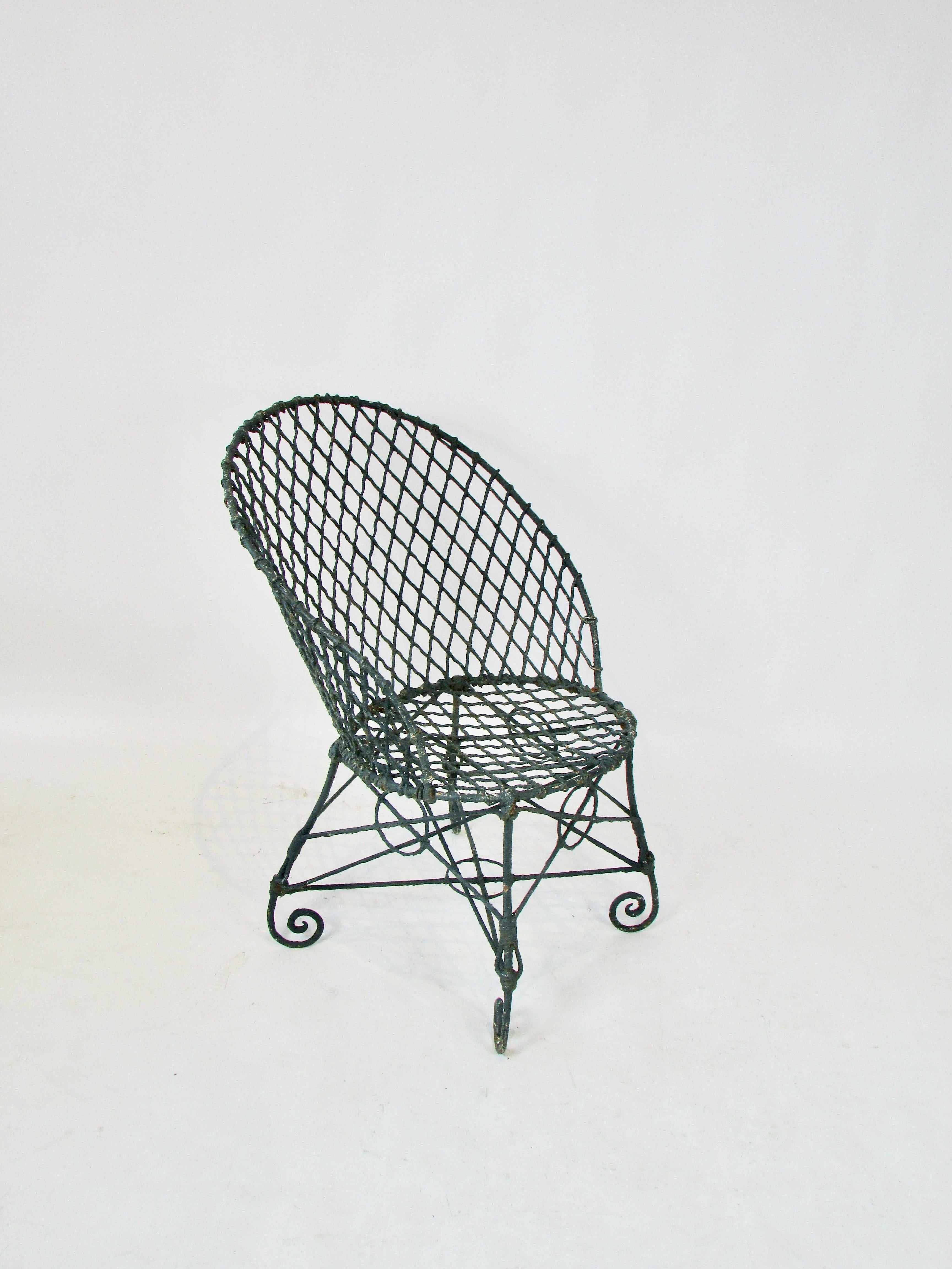Early 20th century wire chair . Wrought iron frame with scrolled feet holds fine intricate wire work frame . Chair probably has many layers of paint . Current color applied years ago has a green tint to it . Plenty of rust and patina as shown .