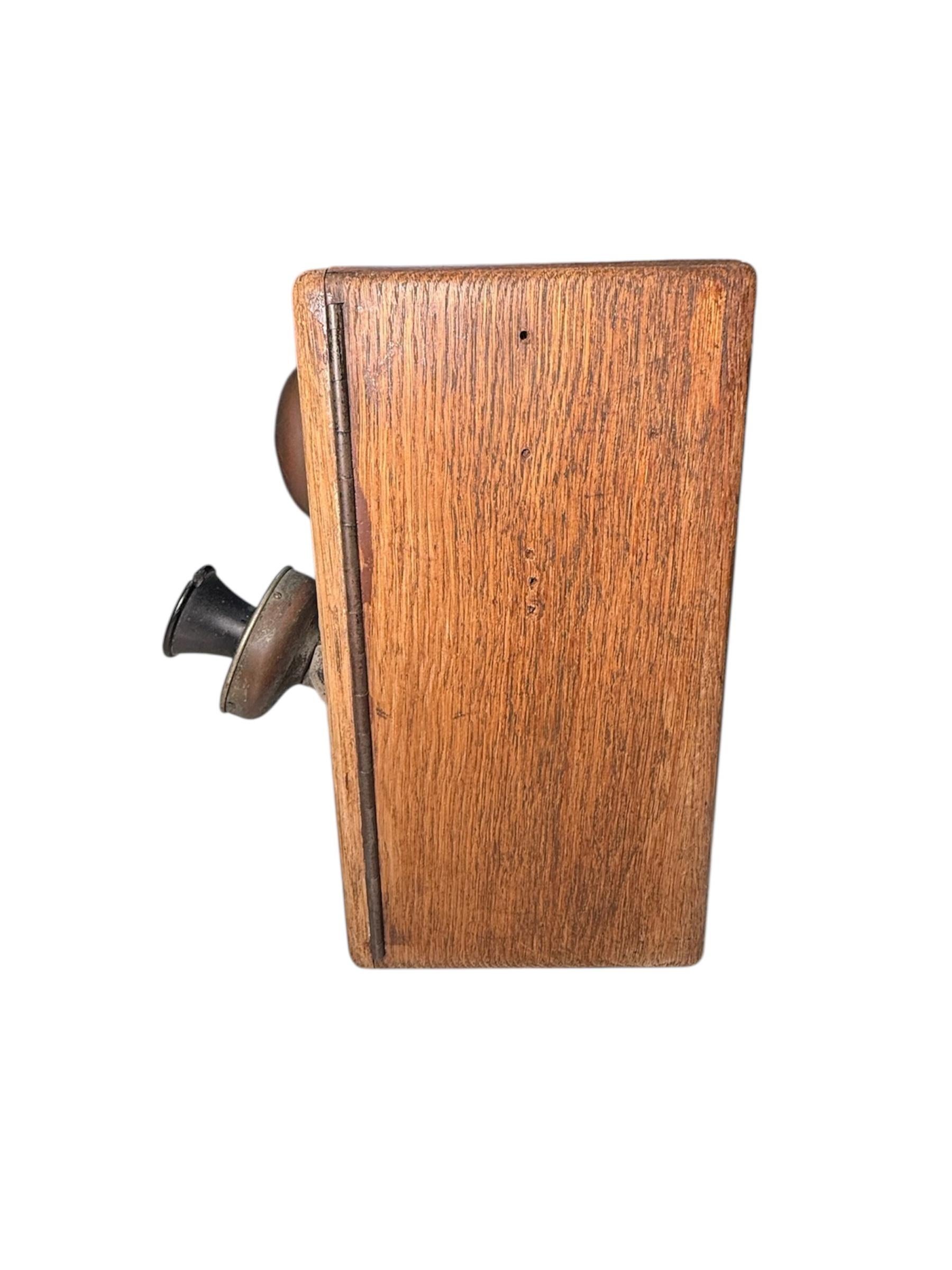 Si tratta di un telefono da parete dei primi del Novecento. Raffigura una scatola di legno di forma rettangolare con campanelli esterni nella parte anteriore e cornetta laterale.
