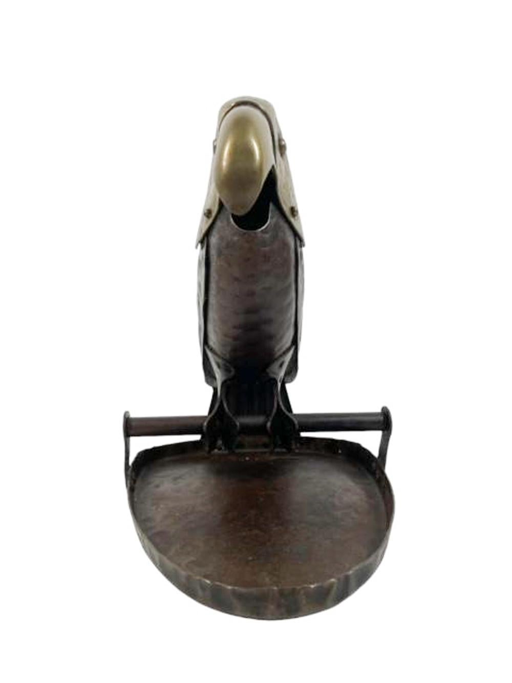 Early 20th century hammered iron and brass tabletop cigar gutter in the form of a full-bodied parrot on a perch attached to a leaf. Made of painted iron with a brass head, the parrots beak clips the tip of a cigar with the use of the feather on top