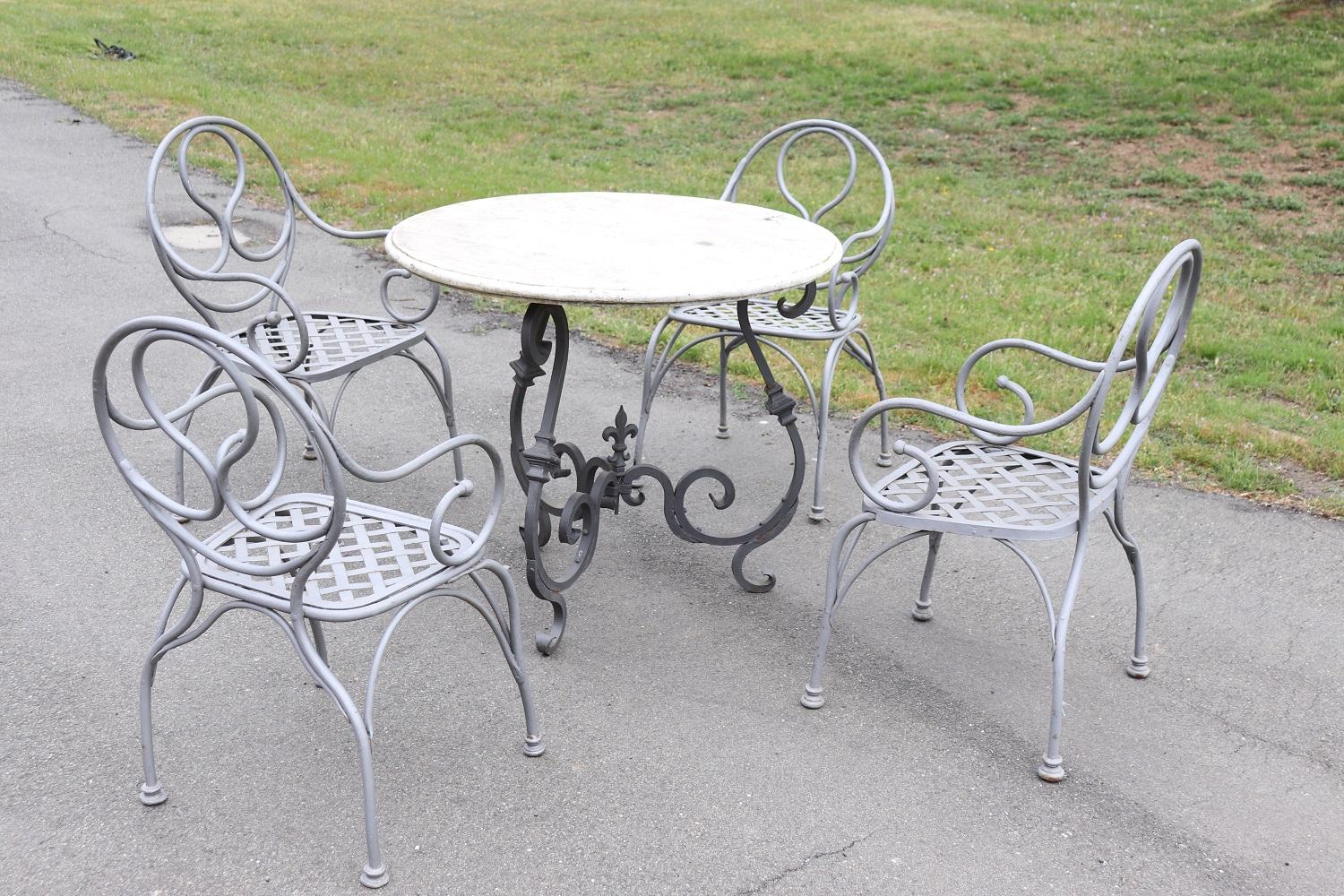 Beautiful refined garden set in neoclassical style, circa 1930s. Four armchairs and a round wrought iron table and fine Italian marble top. Refined iron decoration. The armchairs are large and comfortable with cushions (used). The marble top shows
