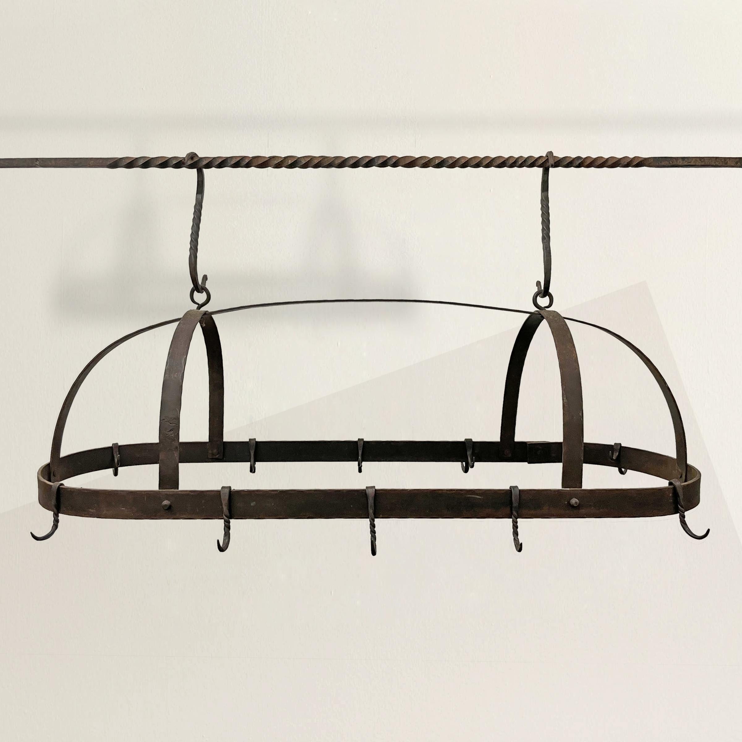 An wonderful early 20th century American hand-wrought iron pot rack constructed from several flat iron bars that are shaped into a rack, and suspended by two large wrought iron twisted S hooks, and two double-hooks each containing a hook on the
