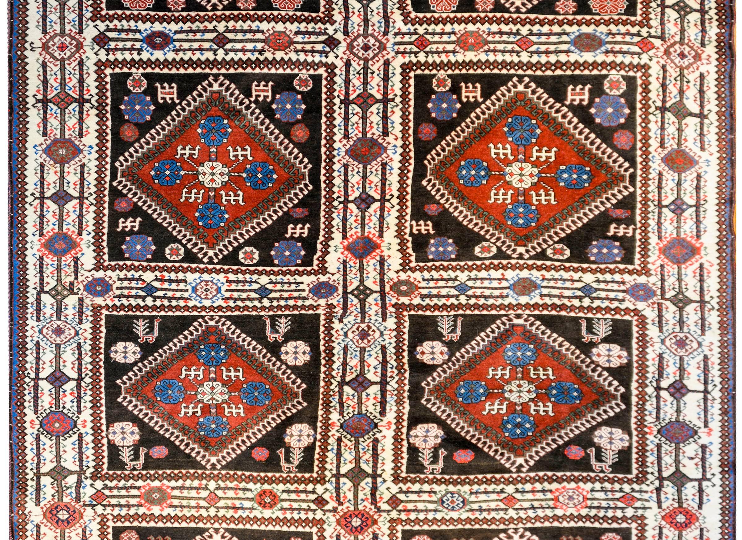 An early 20th century Persian Yalameh rug with eight multicolored geometric diamond-shaped medallions amidst fields of stylized flowers, birds, and goats on a black wool background. The borer is wide with large stylized flowers on a white background.