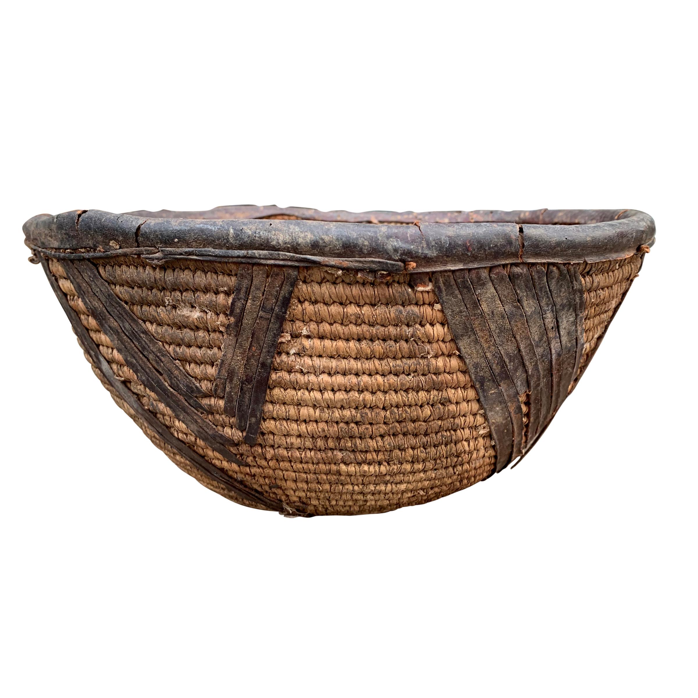 A simple, but chic, early 20th century woven natural fiber basket from the Yoruba People of Nigeria, with leather rim and decorative leather embellishments around the exterior.