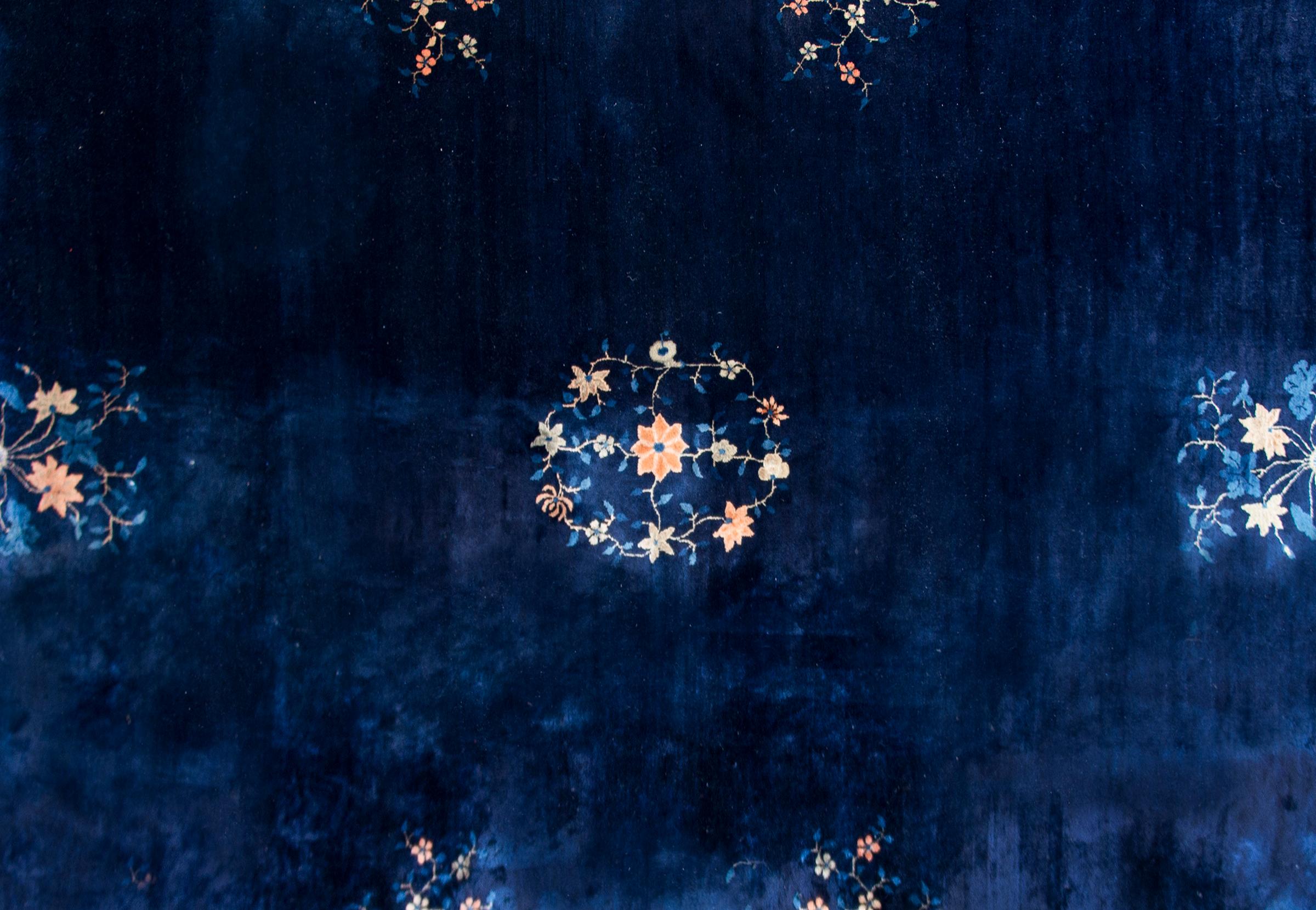Magnifique tapis chinois de Pékin du début du XXe siècle au motif simple contenant un médaillon floral central sur un fond indigo foncé, entouré d'une large bordure indigo clair et couvert de fleurs plus propices.