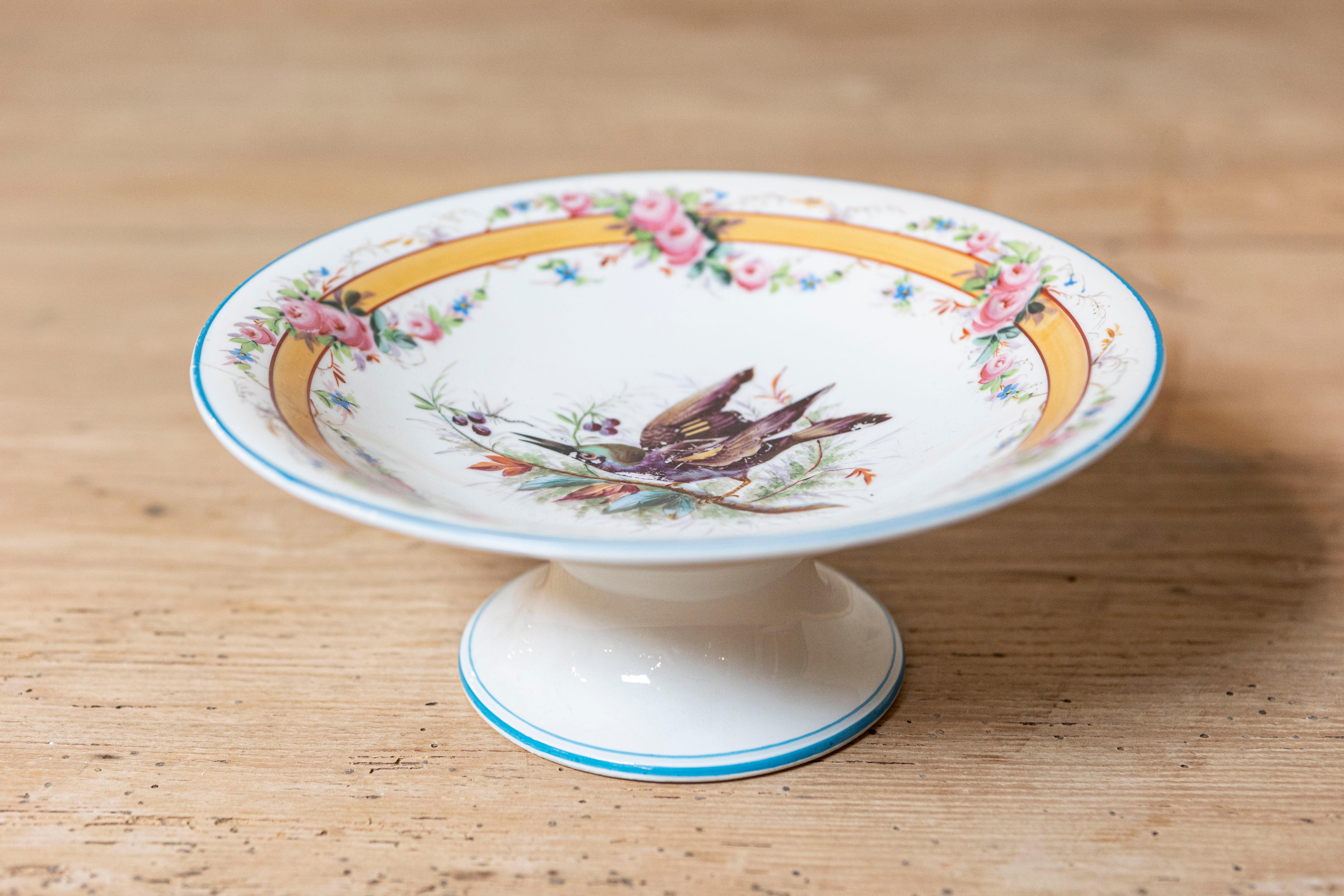 A beautifully hand-painted porcelain compote dish featuring an elegant pedestal form and richly detailed decoration. The interior showcases a pair of birds perched among delicate foliage, rendered in fine brushwork and naturalistic colors.