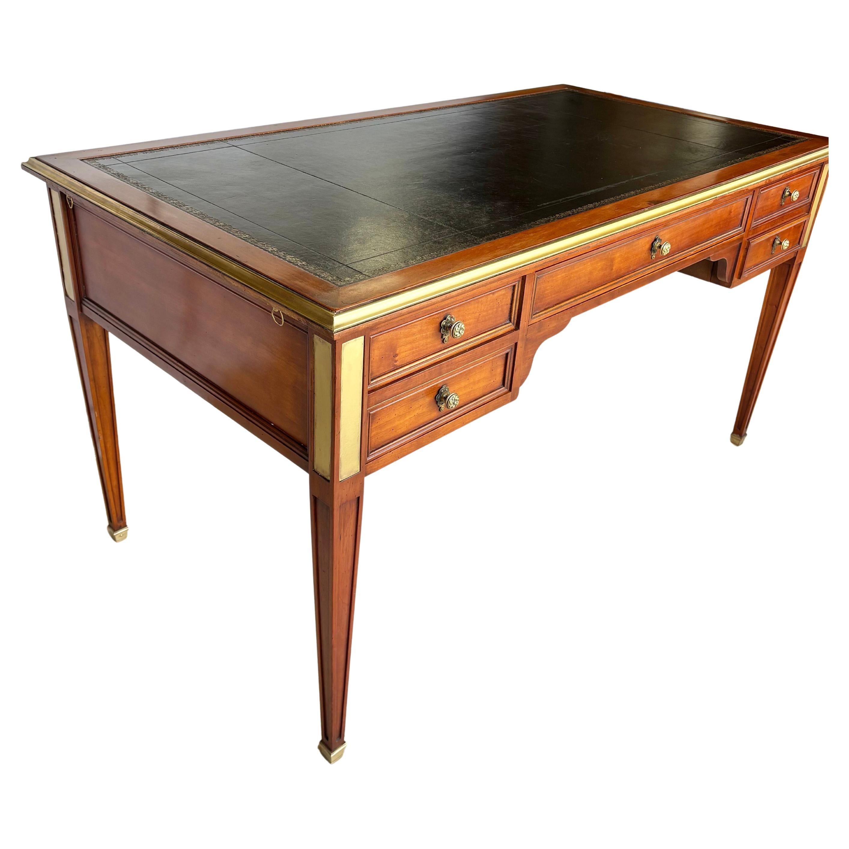 Found in France, this Early 20th Century Writing Desk was crafted from Cherrywood by French artisans in the early 1900's in the Louis XVI style. The piece features a tooled leather top bordered with brass and two leather pull out extensions located