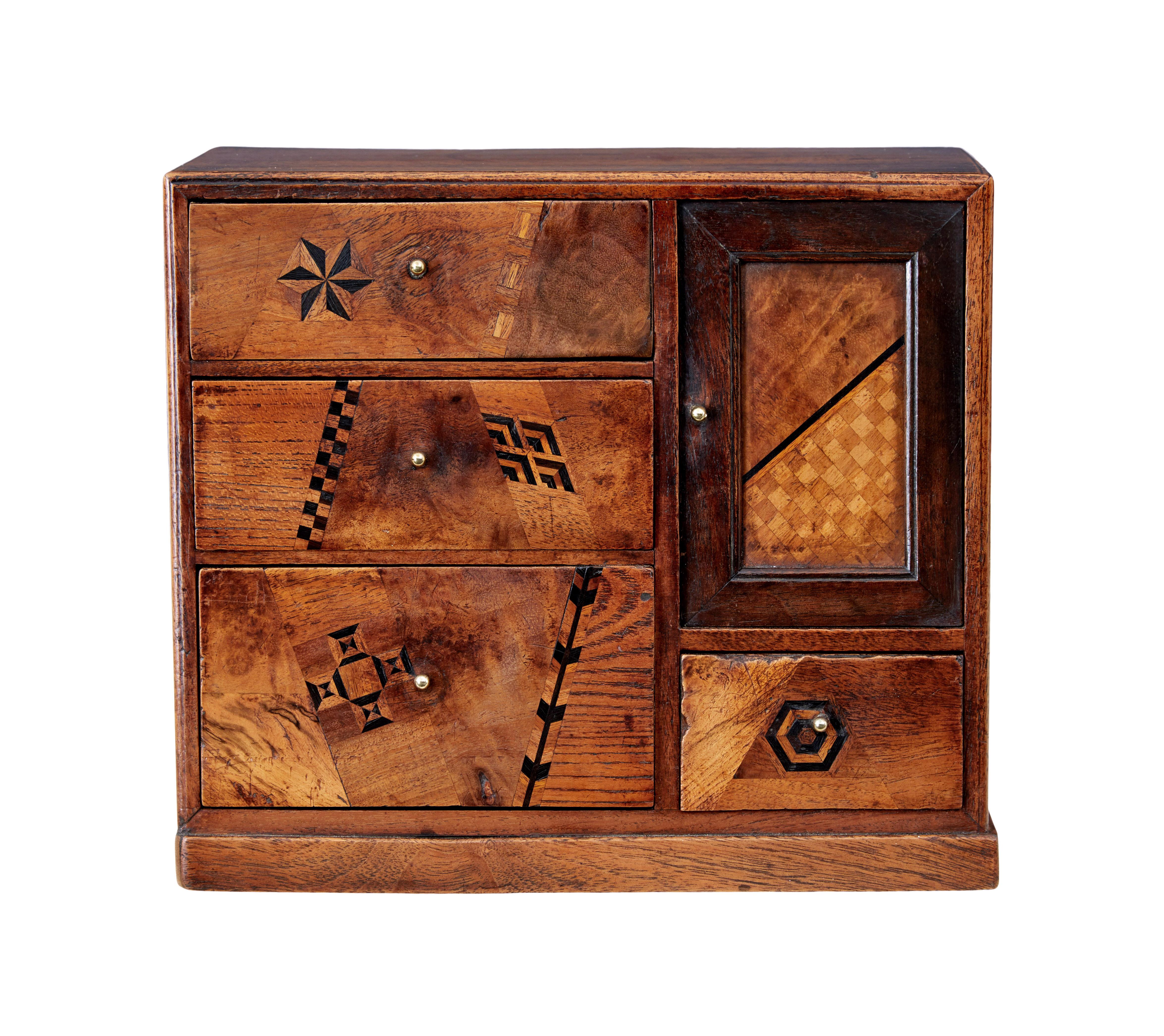 Early 20th inlaid desktop drawer cabinet circa 1910.

Unusual small apprentice piece. Made using various woods and showcasing various techniques of inlay and woodwork.

A bank of 3 graduating drawers to the left and a sliding door to the left with 2