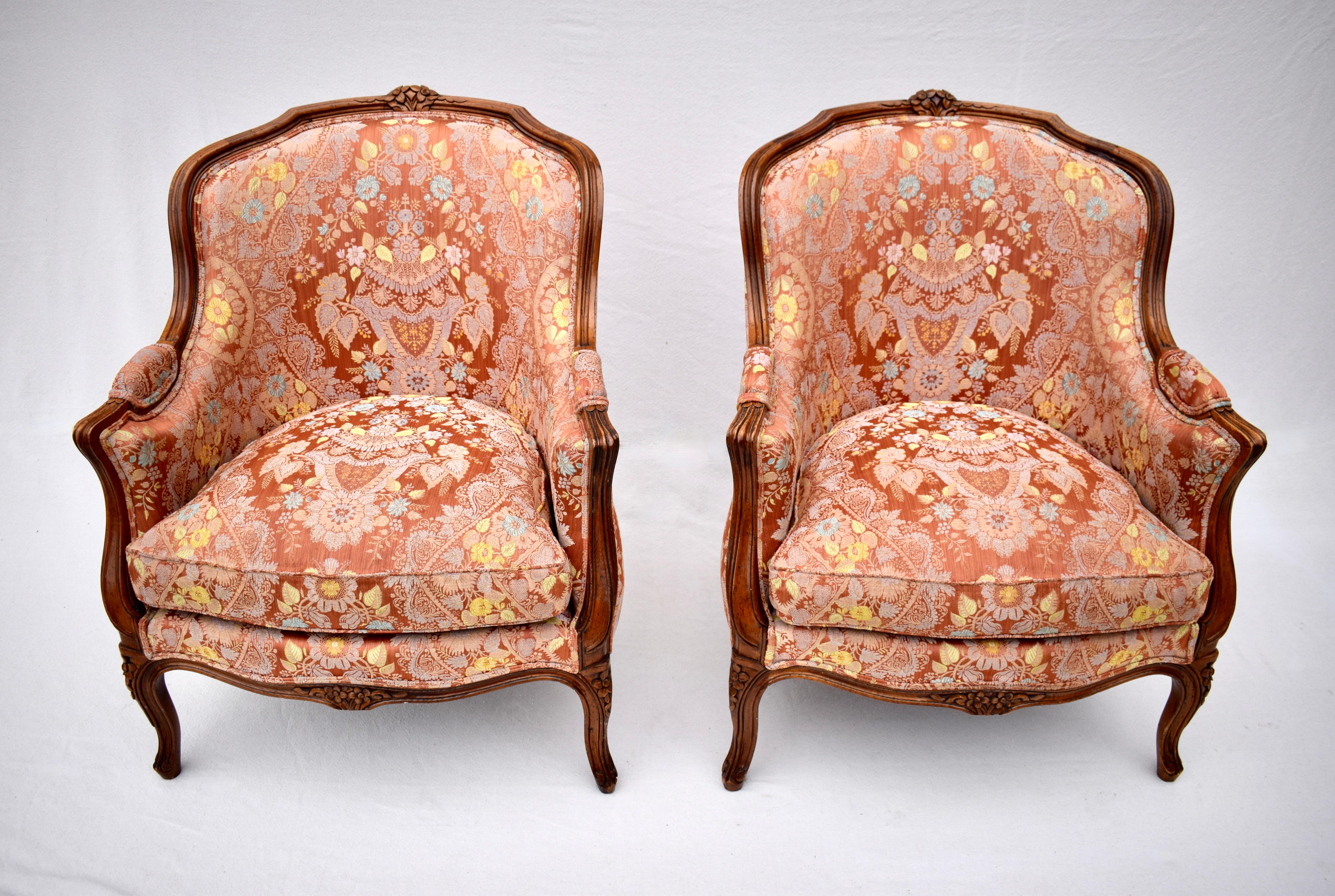 A pair of Louis XV style Bergere chairs of solid carved walnut refinished to their natural color. Reupholstered in the late 1990's in gorgeous multi Salmon Damask floral fabric with plush goose down cushions. Beautifully maintained in rarely used