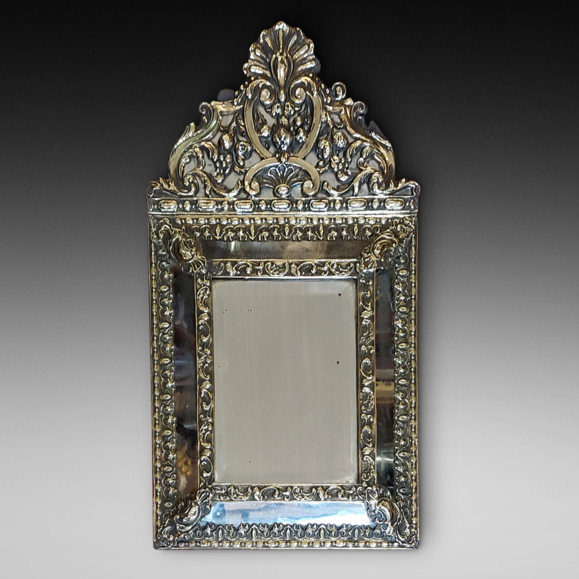 Miroir mural de style hollandais du début du 19e siècle - la plaque oblongue biseautée est logée dans un cadre en laiton surmonté d'une arche gaufrée de feuillage avec une crête ornée d'une coquille - 12,5 