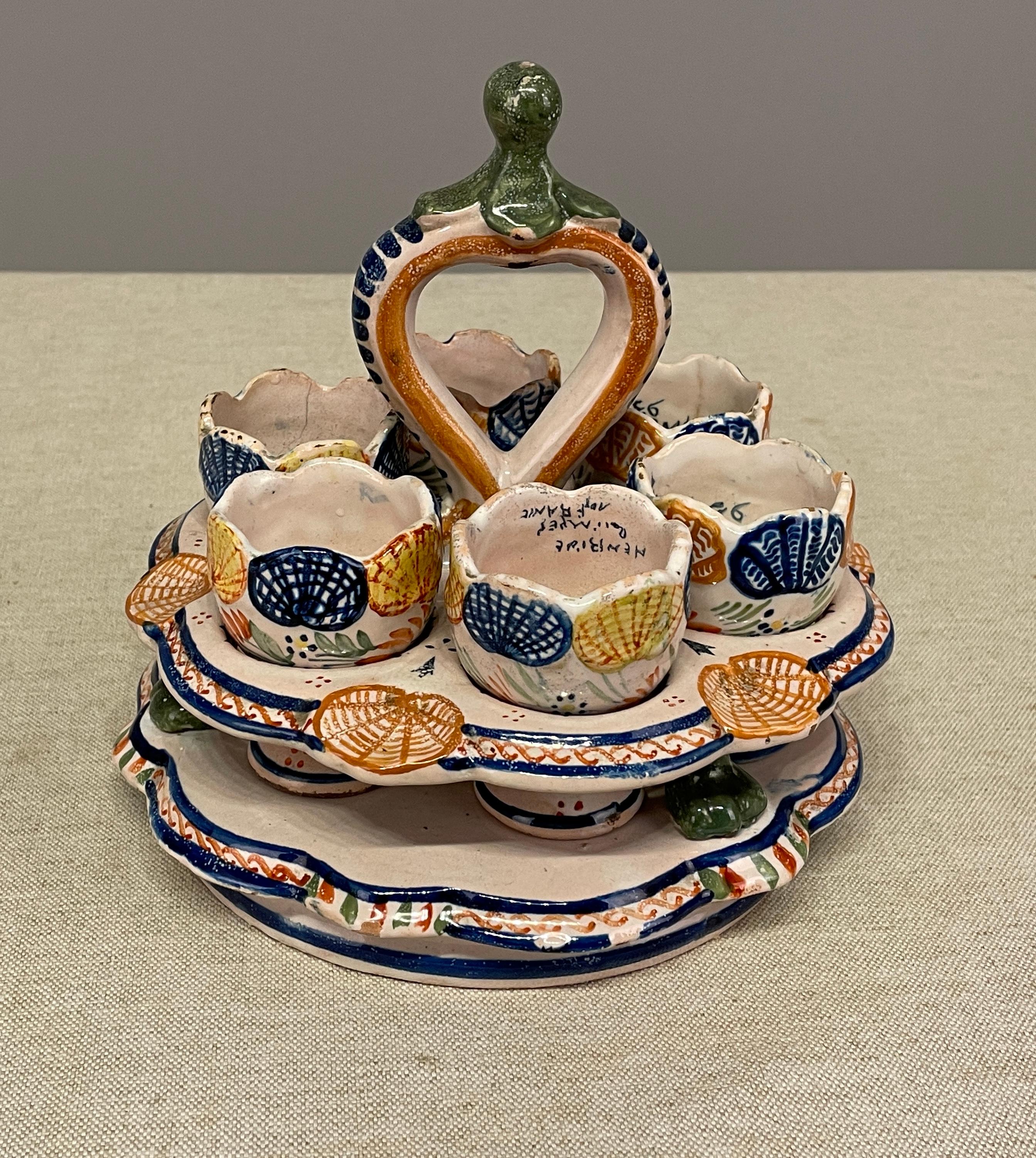 An early 20th c French faience from Henriot Quimper, a basket with 6 egg cups in the typical color and pattern from Brittany. 
Note that one chip and one hair line on cup holder. 
Dimensions are 7