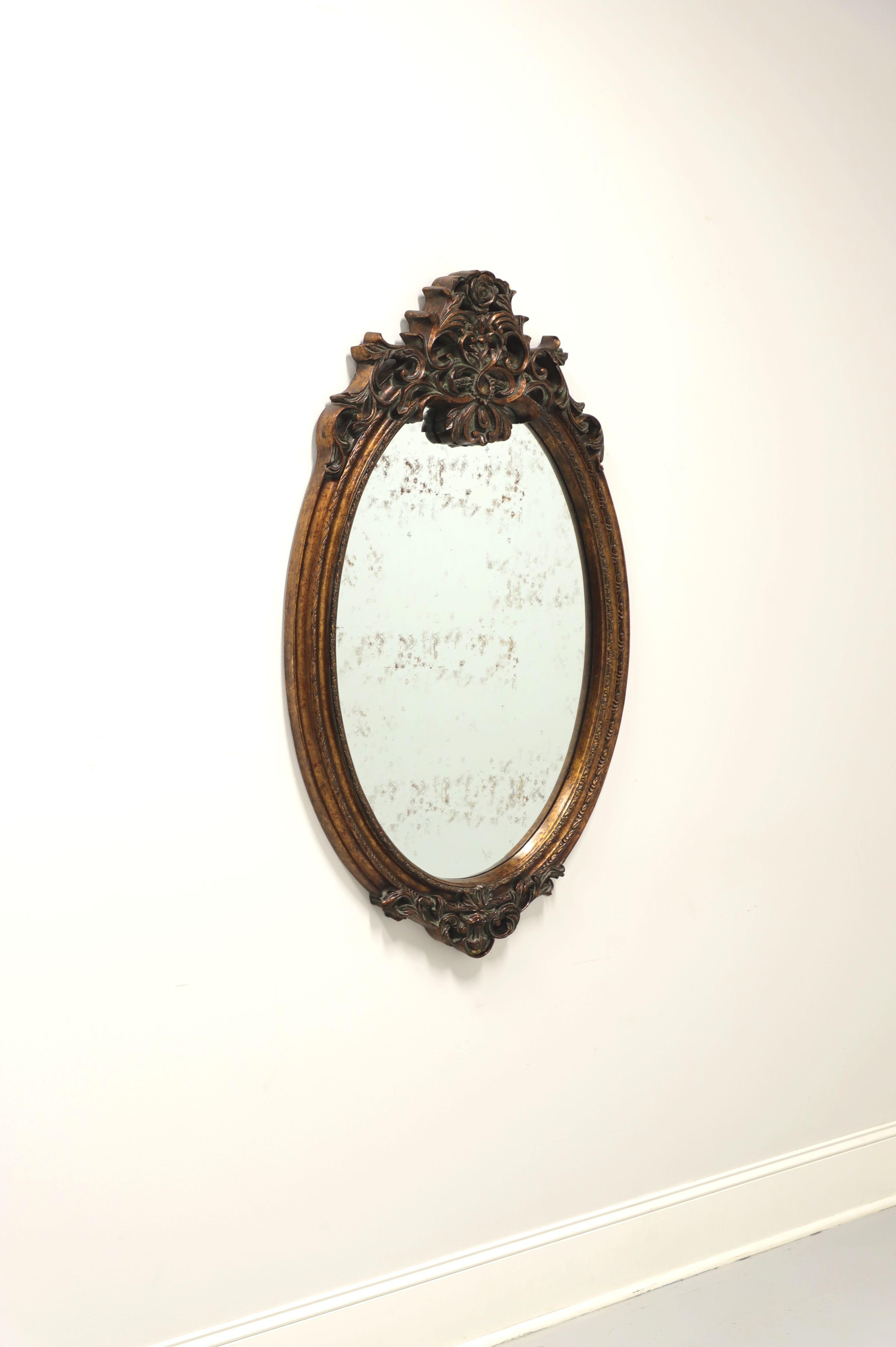 A Baroque style oval wall mirror, unbranded. Mirrored glass intentionally silvered to make appear aged with a sculpted foam frame painted bronze. Features ornate floral carving to top and bottom. Likely made in the USA, in the early 21st