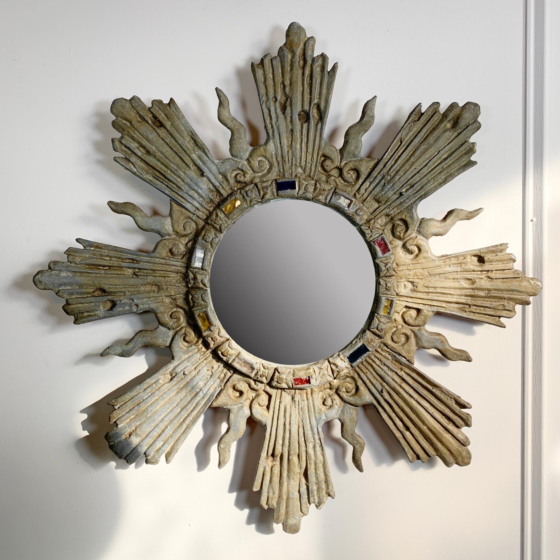 A heavy hand crafted lead sunburst mirror, the hammered and shaped rays stretch out from the central circular foxed mirror, which is decorated with a ring of coloured glass, very much in the manner of Line Vautrin.

French and dating to the