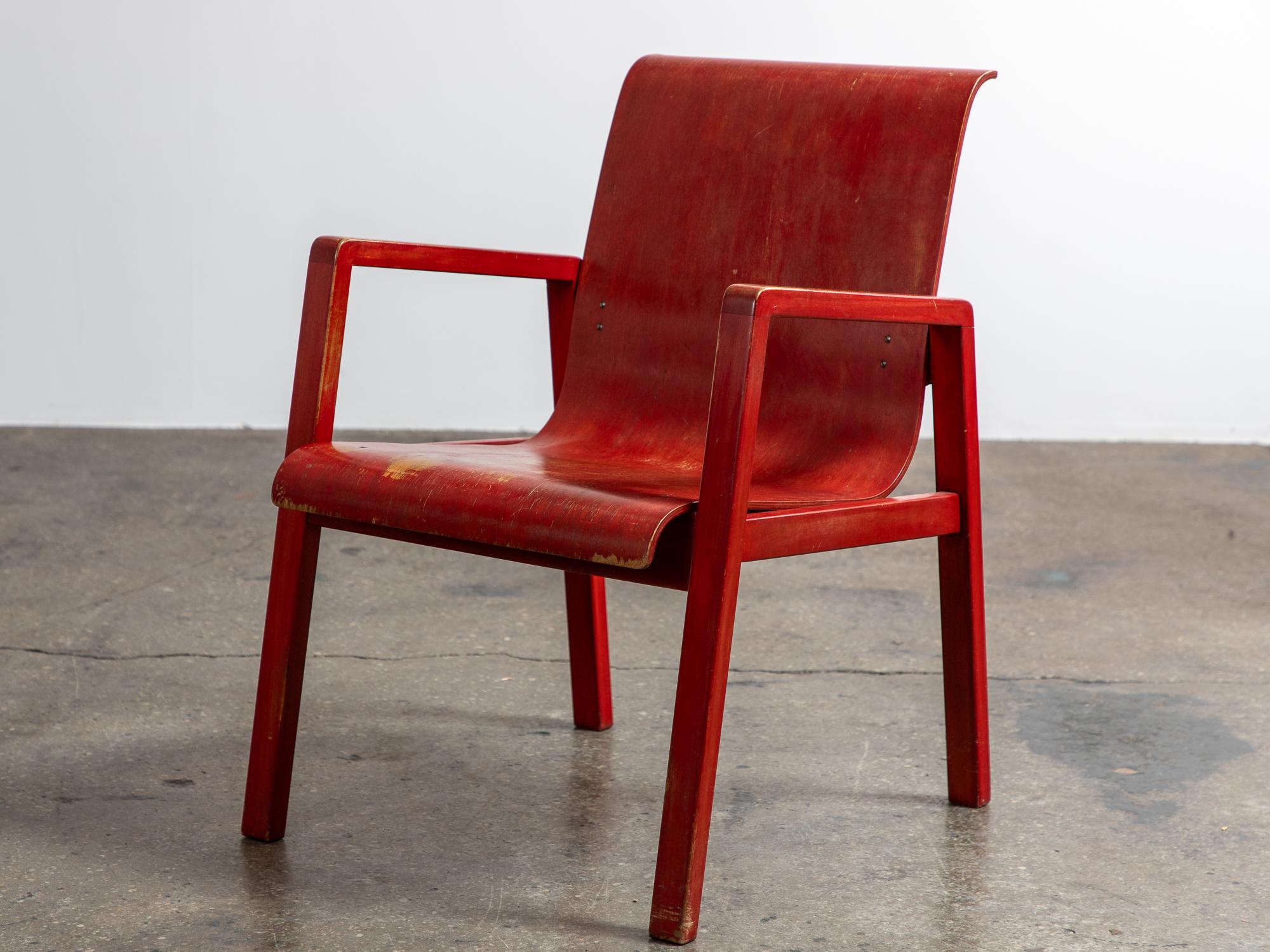 Remarquable chaise de couloir modèle 403 en laque rouge, conçue par Alvar Aalto pour le sanatorium de Paimio, plus tard éditée par Finmar. Le fauteuil présente un design fluide, avec une assise et un dossier en contreplaqué gracieusement incurvés,